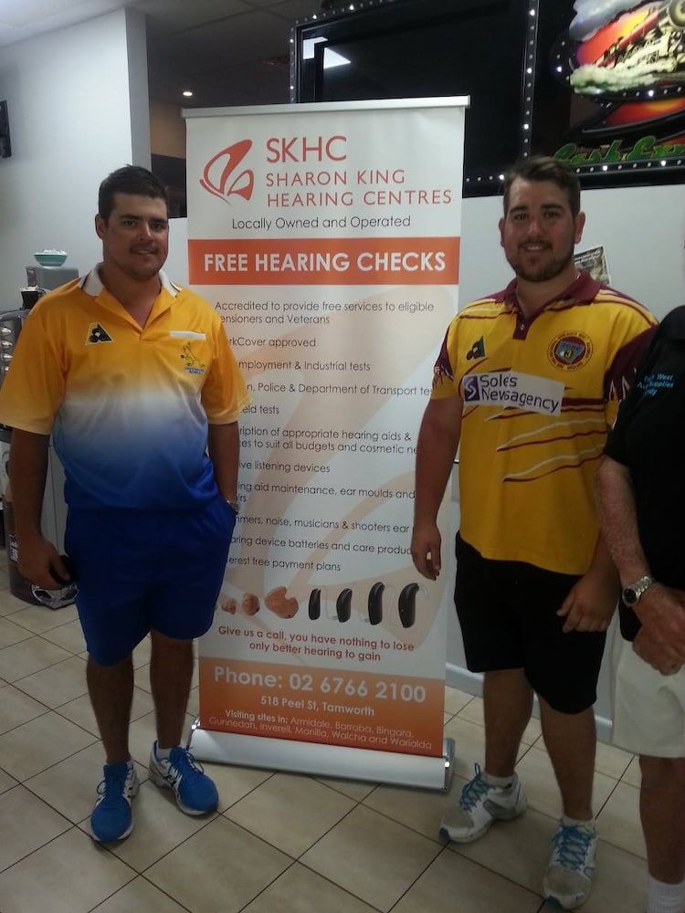 Two Men Standing In Front Of A Sign That Says Free Hearing Checks — Inverell Sporties in Inverell, NSW