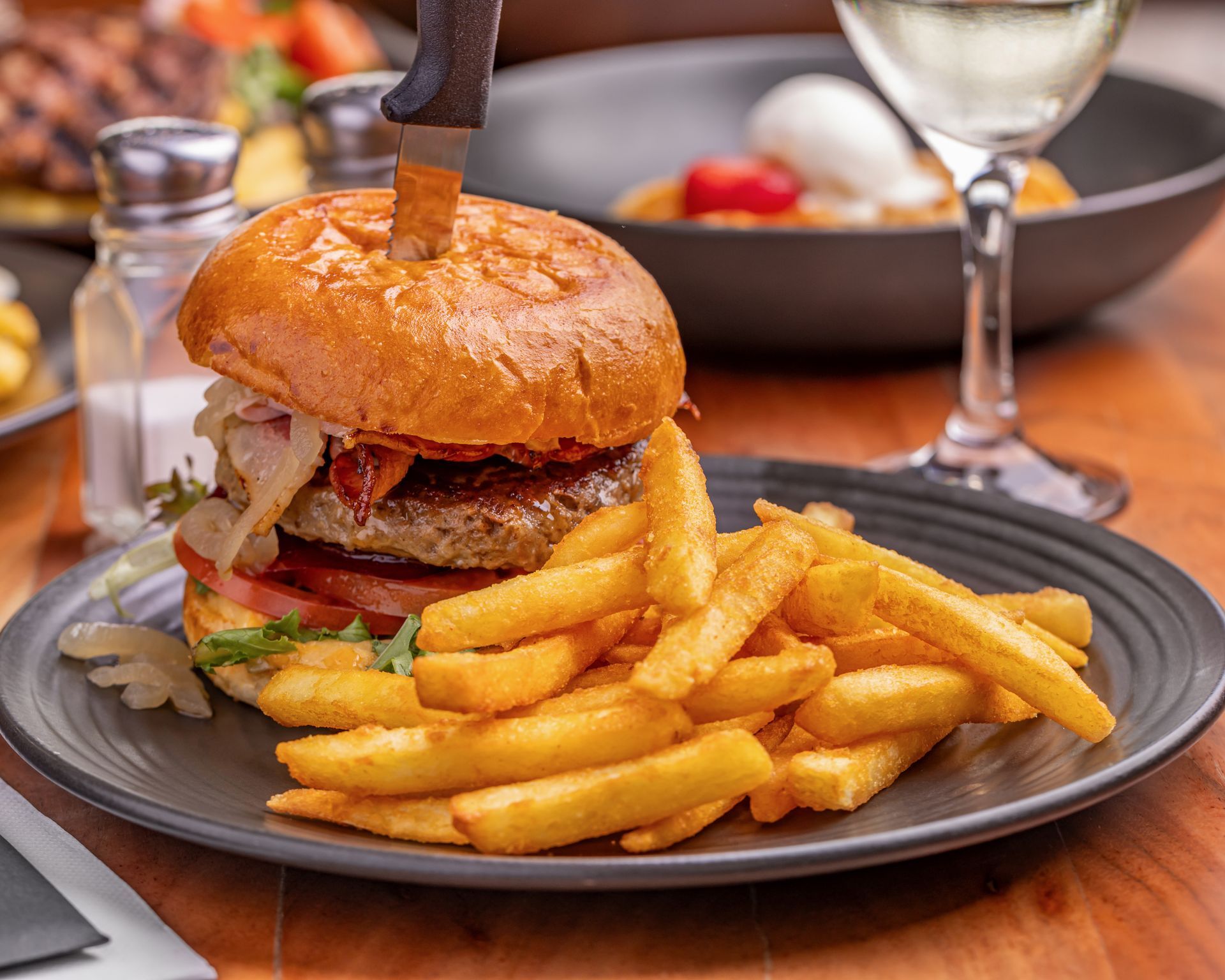 Burger with fries on a plate, knife through the burger, with a glass of white wine. — Inverell Sporties in Inverell, NSW