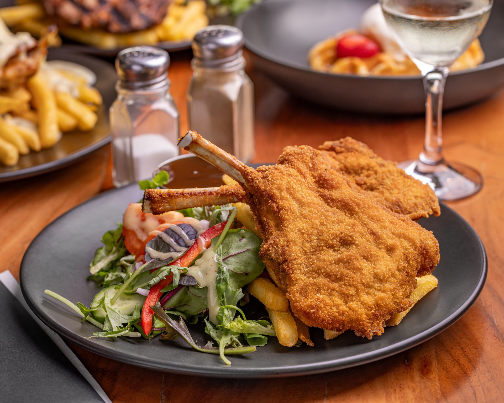 Breaded Pork Chops, Fries, and Salad on a Plate, With Wine and Other Dishes in the Background — Inverell Sporties in Inverell, NSW