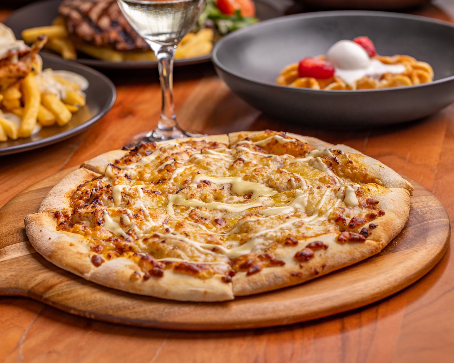 Pizza on a wooden board with other dishes and a glass of wine on a table. — Inverell Sporties in Inverell, NSW