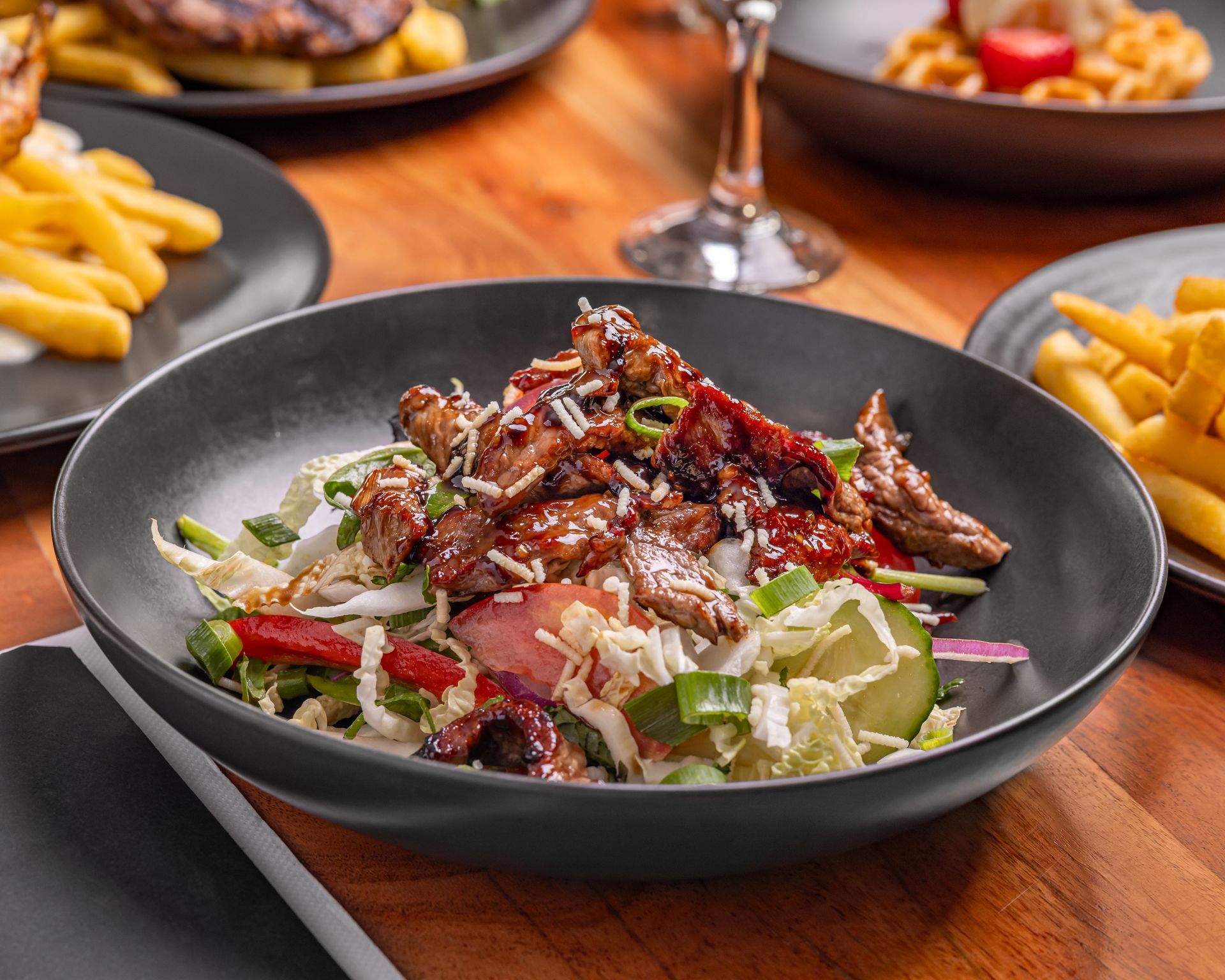 Black bowl with salad topped with meat, on wooden table. — Inverell Sporties in Inverell, NSW