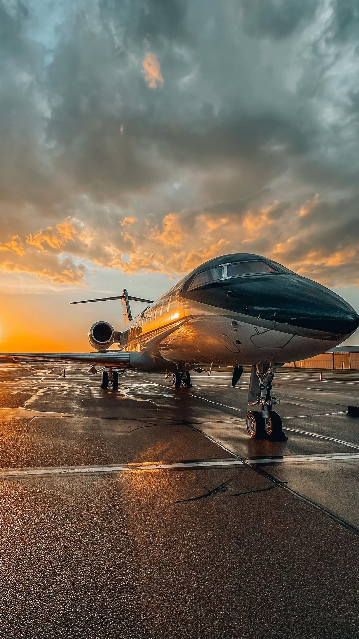 A private jet is parked on a wet runway at sunset.