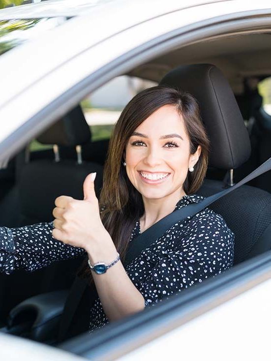 A woman is giving a thumbs up while sitting in a car.