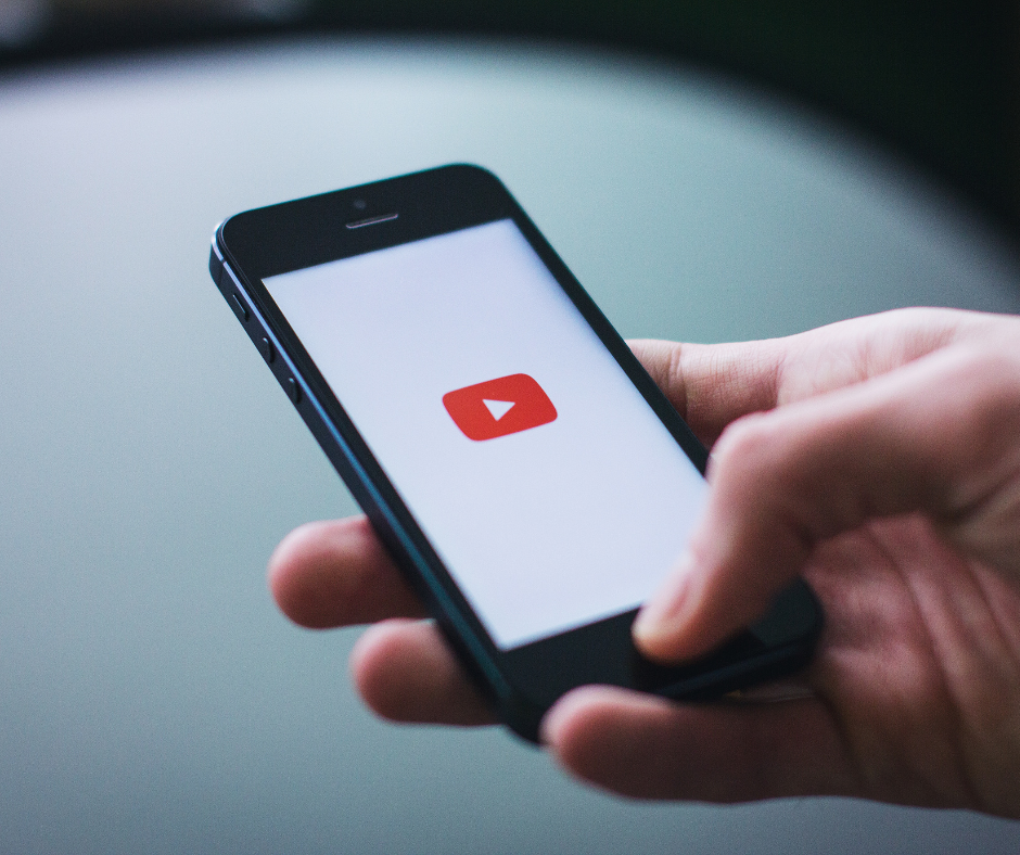 A person is holding a cell phone with a youtube logo on the screen