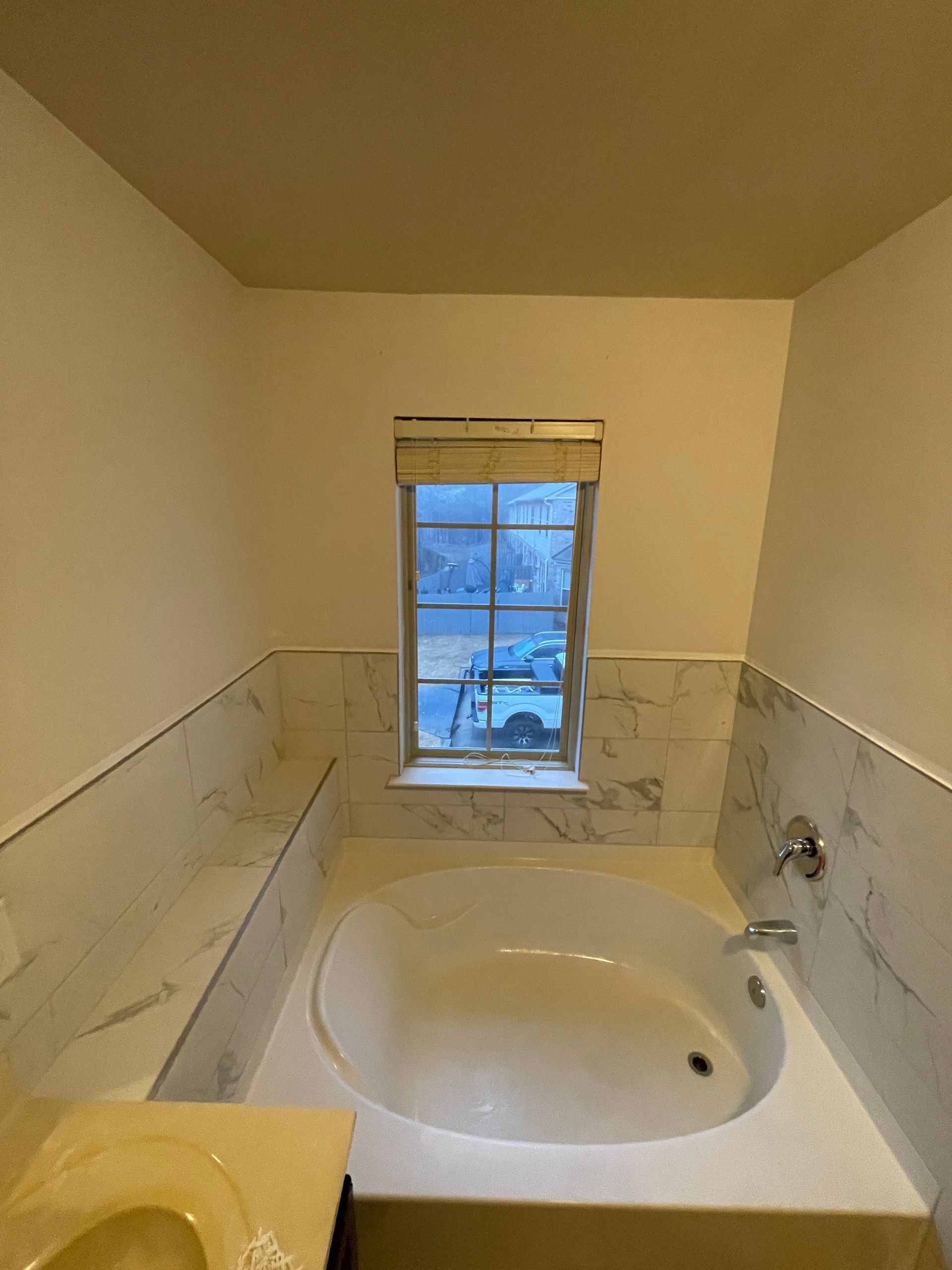 Bathroom with a bathtub, window, and marble tile.