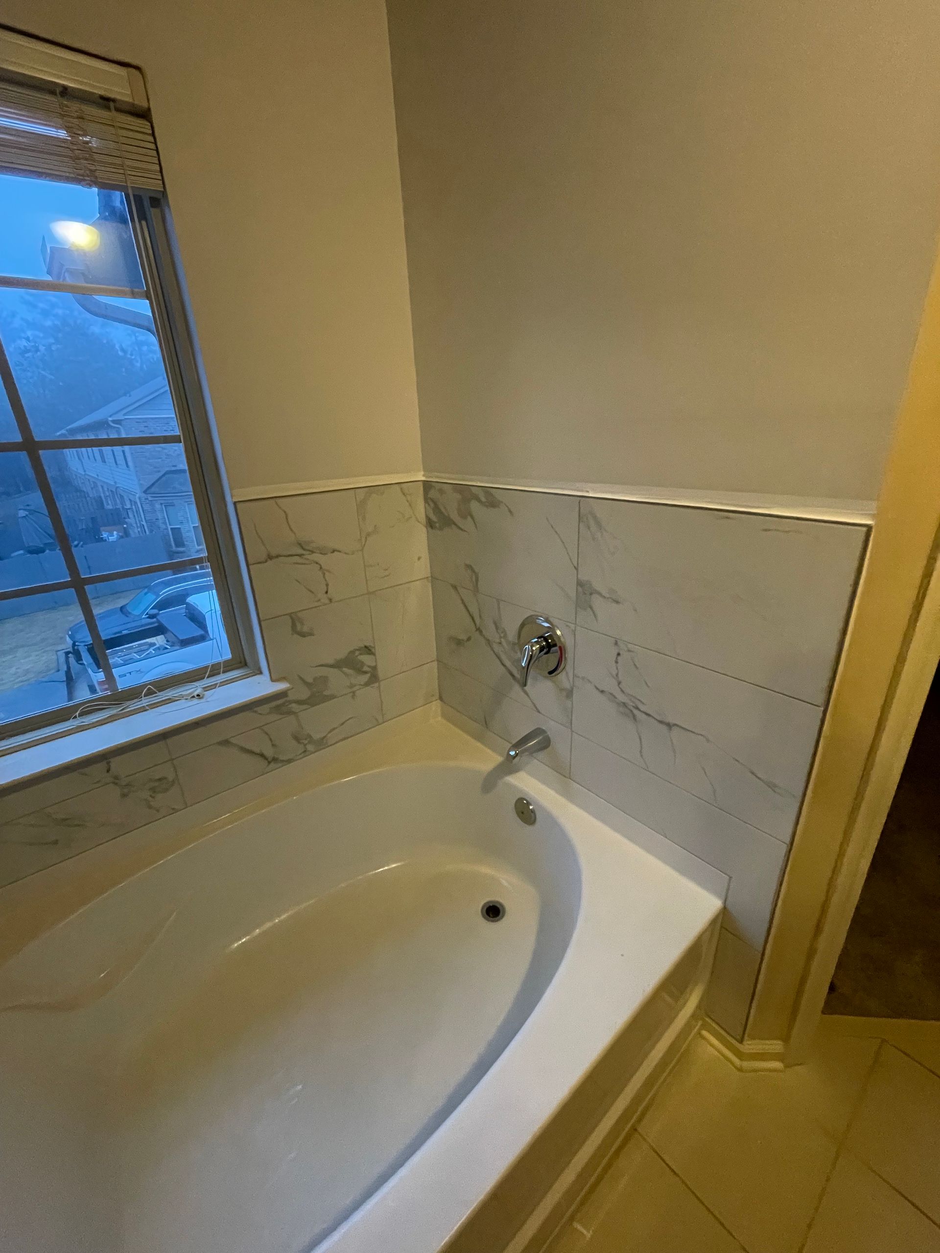 Bathroom with white tub, marble tile, window, and chrome faucet.