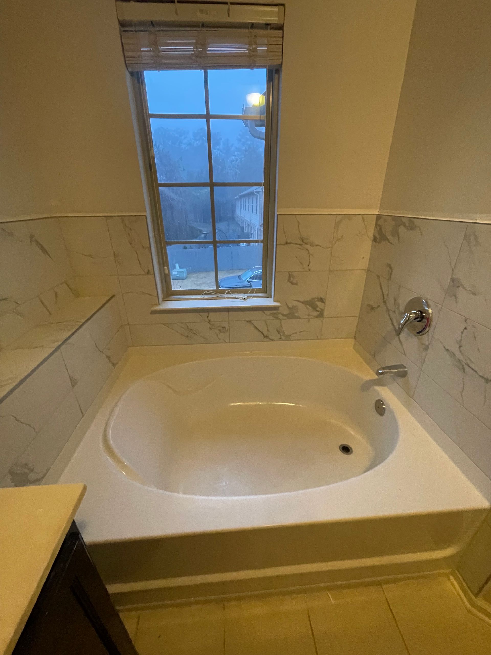 Bathroom with white oval bathtub, marble tile, and a window with a view.