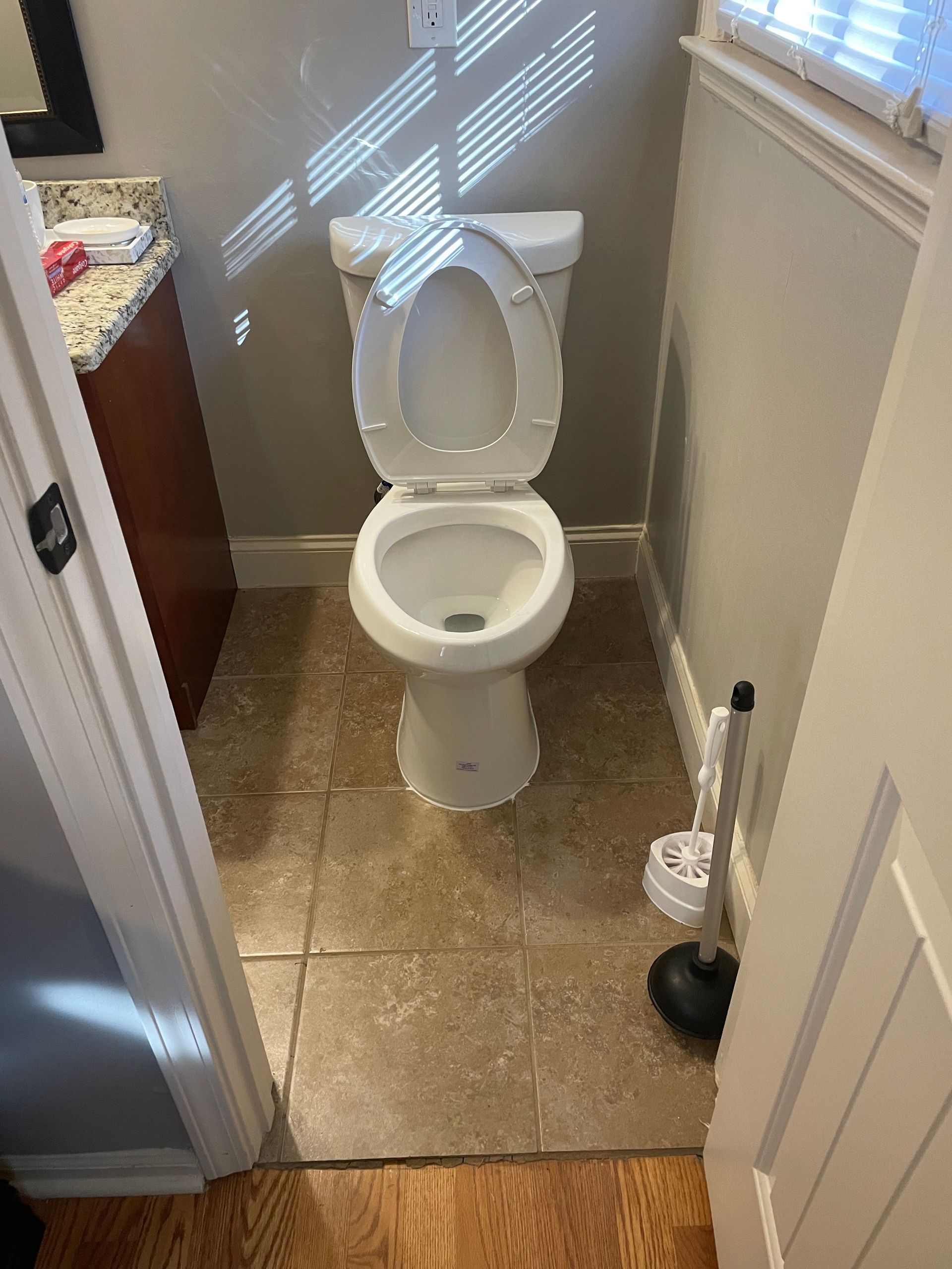 Bathroom with a white toilet, tile floor, and a toilet brush.