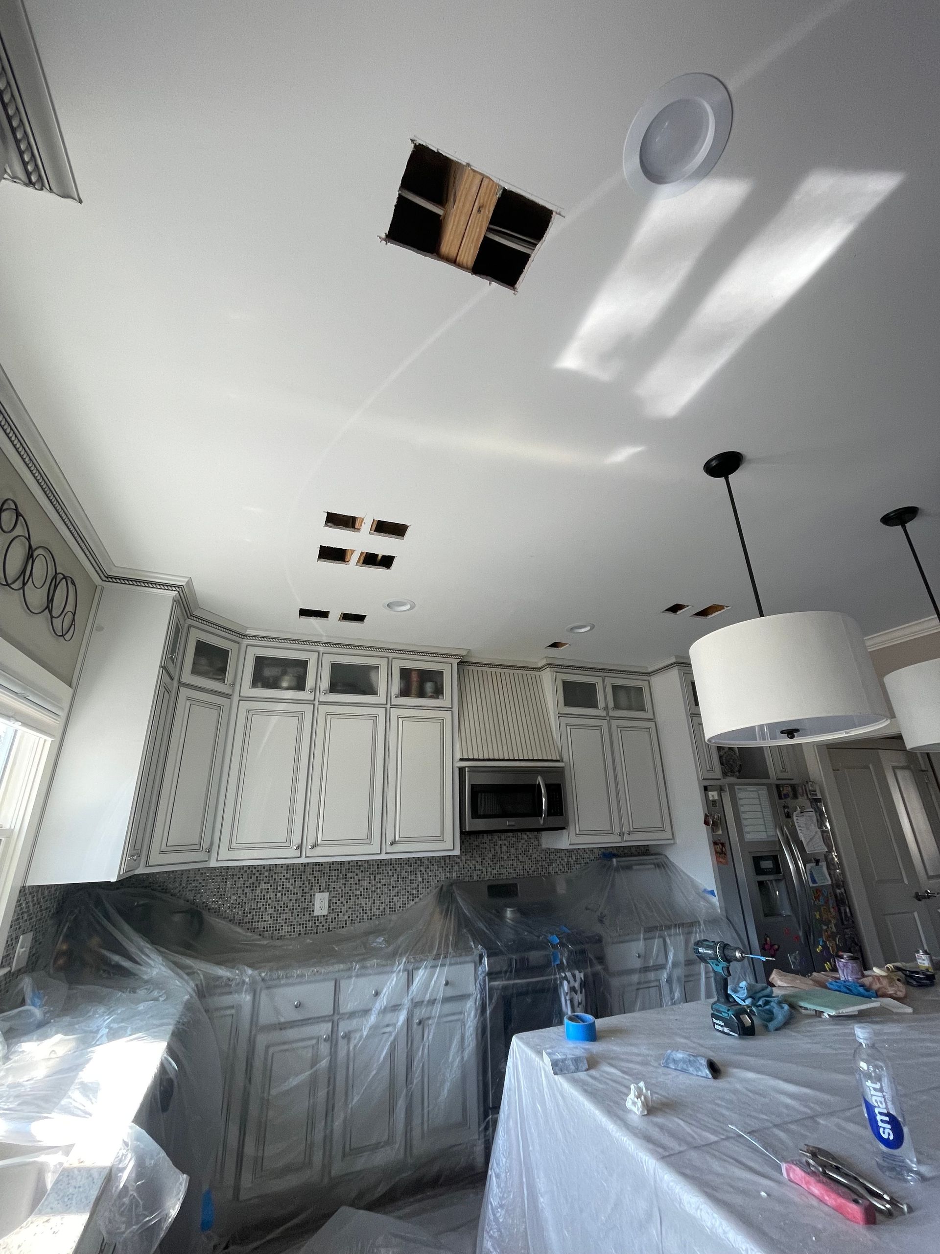 Kitchen with white cabinets, holes in the ceiling for lights, and protective plastic covering surfaces.