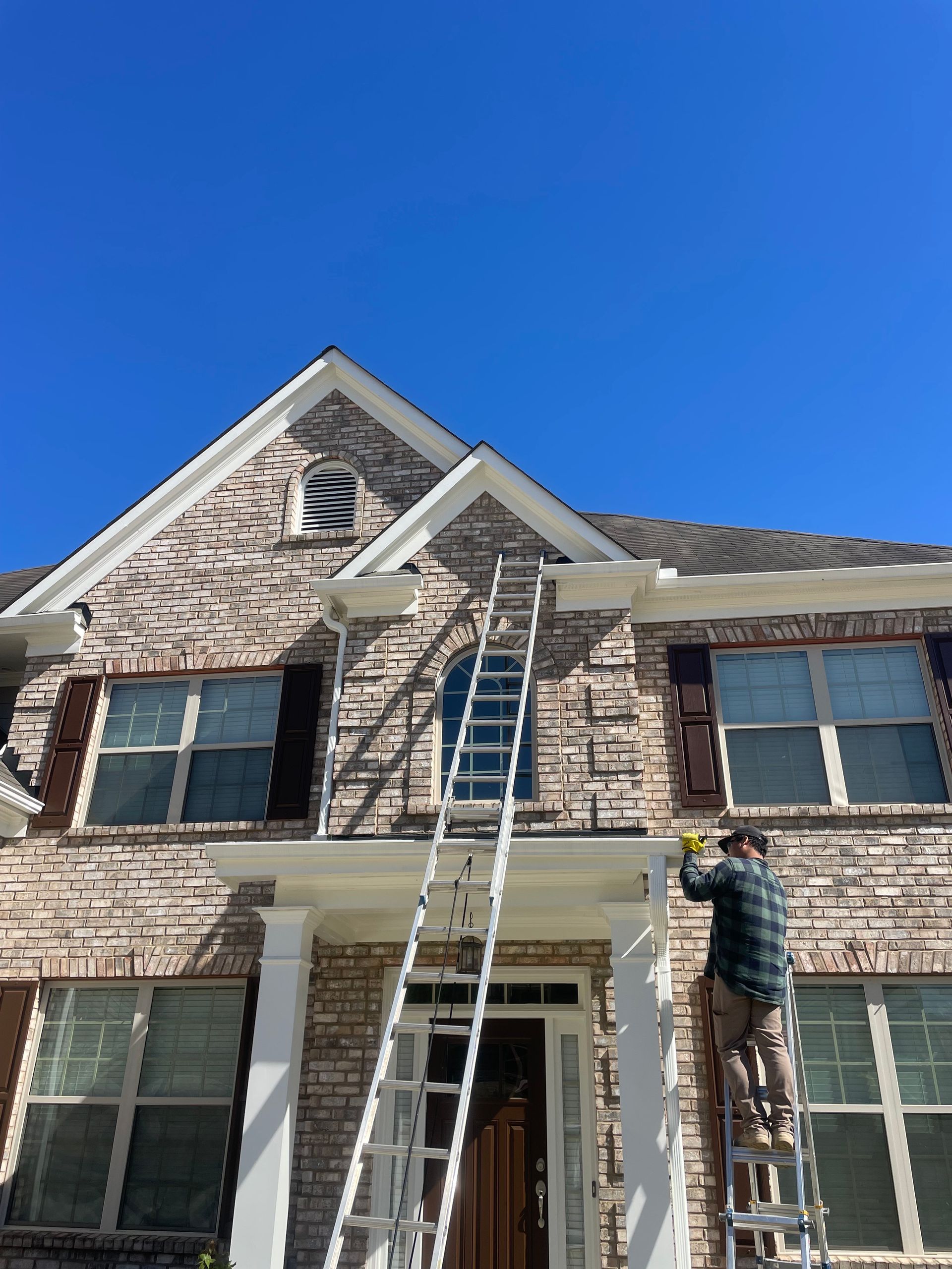 Person on ladder, working on the front of a brick house. Blue sky overhead.