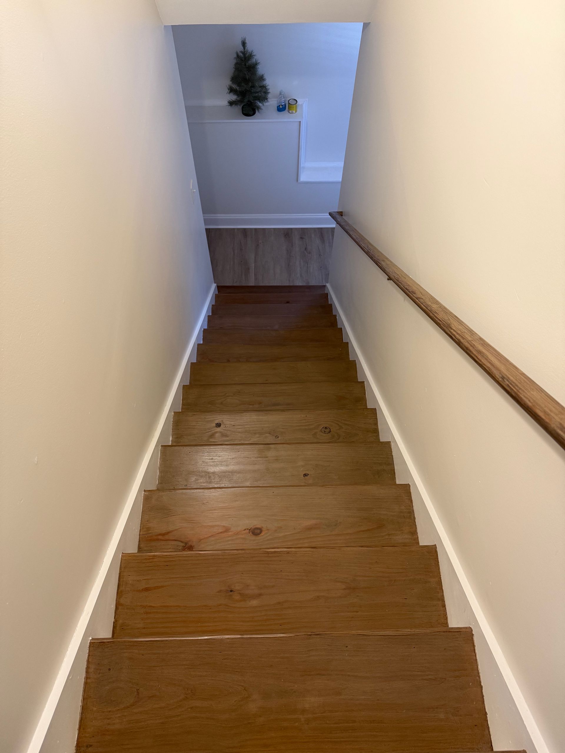 Staircase leading downwards; wood steps with white trim, wood handrail on right, cream-colored walls.
