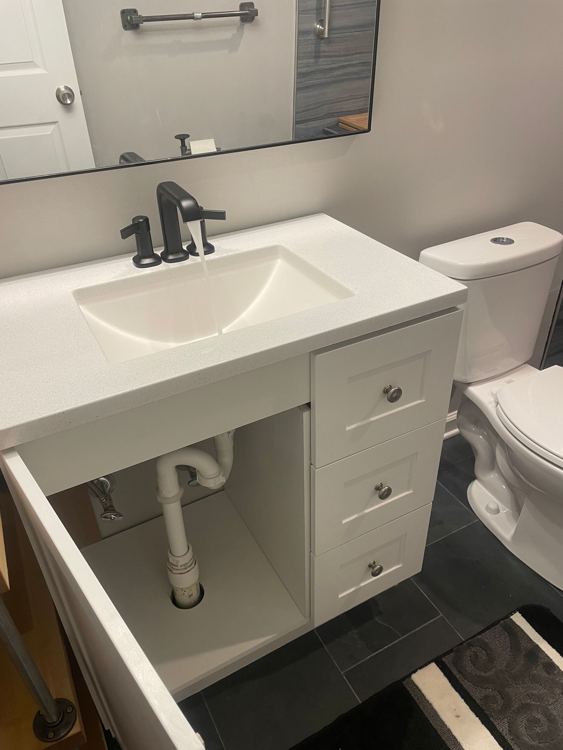 White bathroom vanity with a sink, drawers, and open cabinet door. Toilet is to the right.
