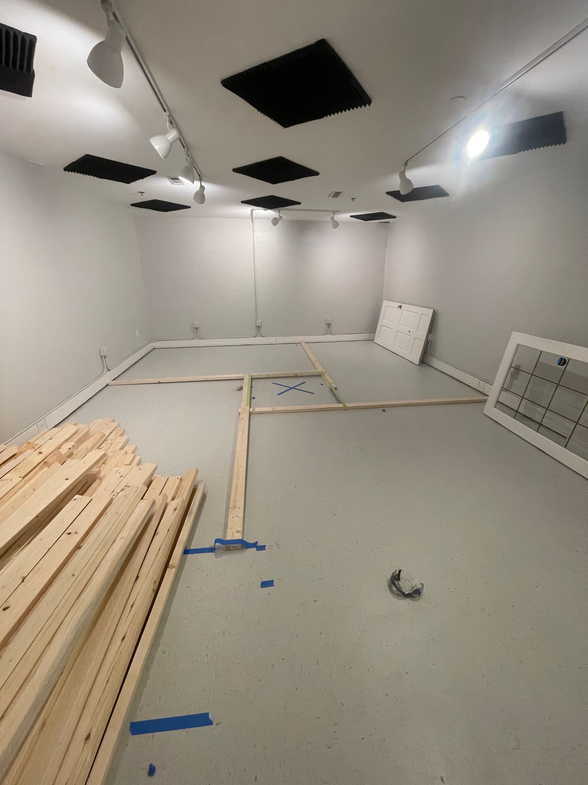 Empty room under construction with wood planks, gray floor, white walls and ceiling, and black vents.
