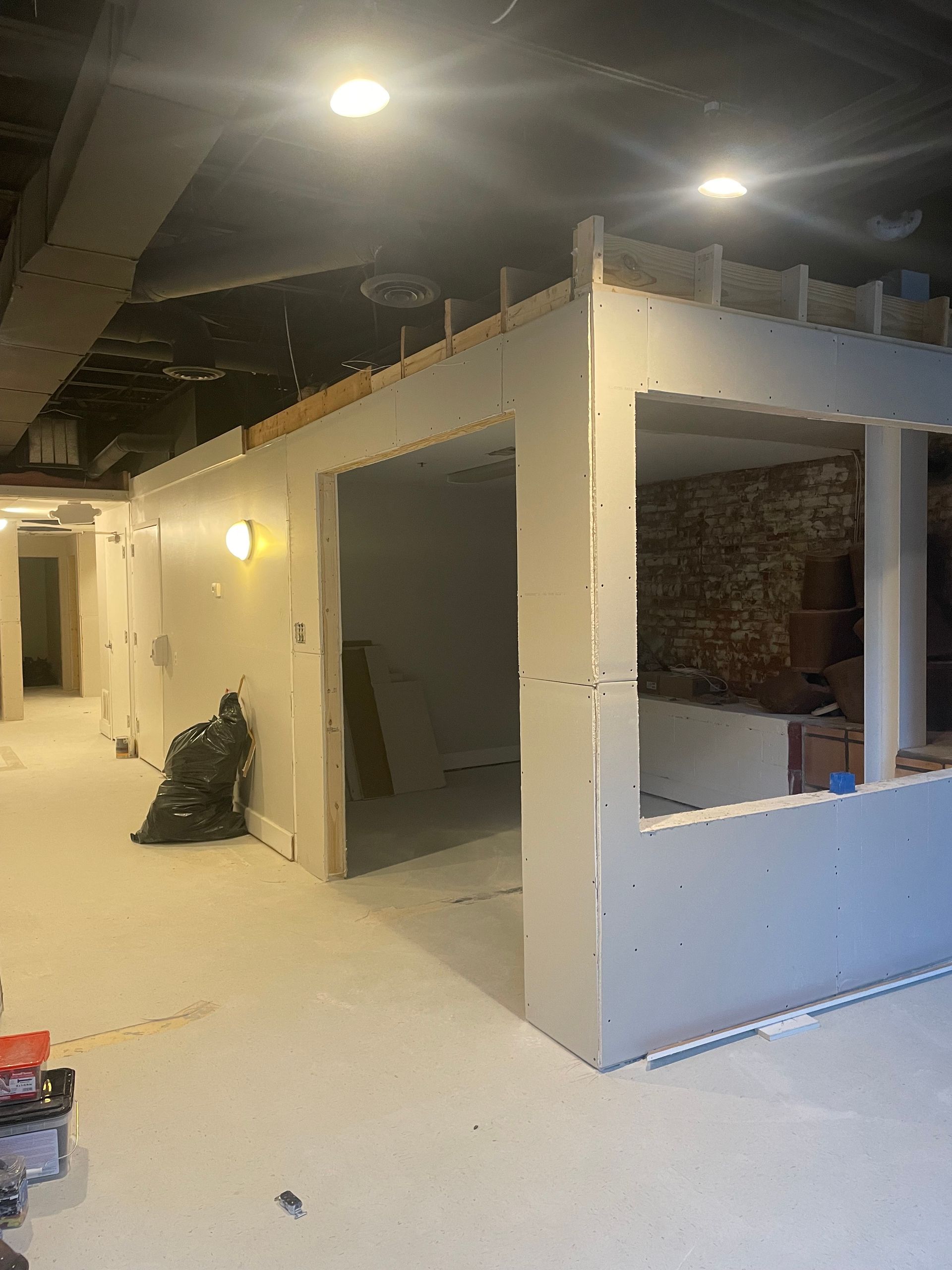 Basement renovation: Drywall installed, unfinished doorway, exposed brick wall visible through opening. Basement renovation: Drywall installed, unfinished doorway, exposed brick wall visible through opening.