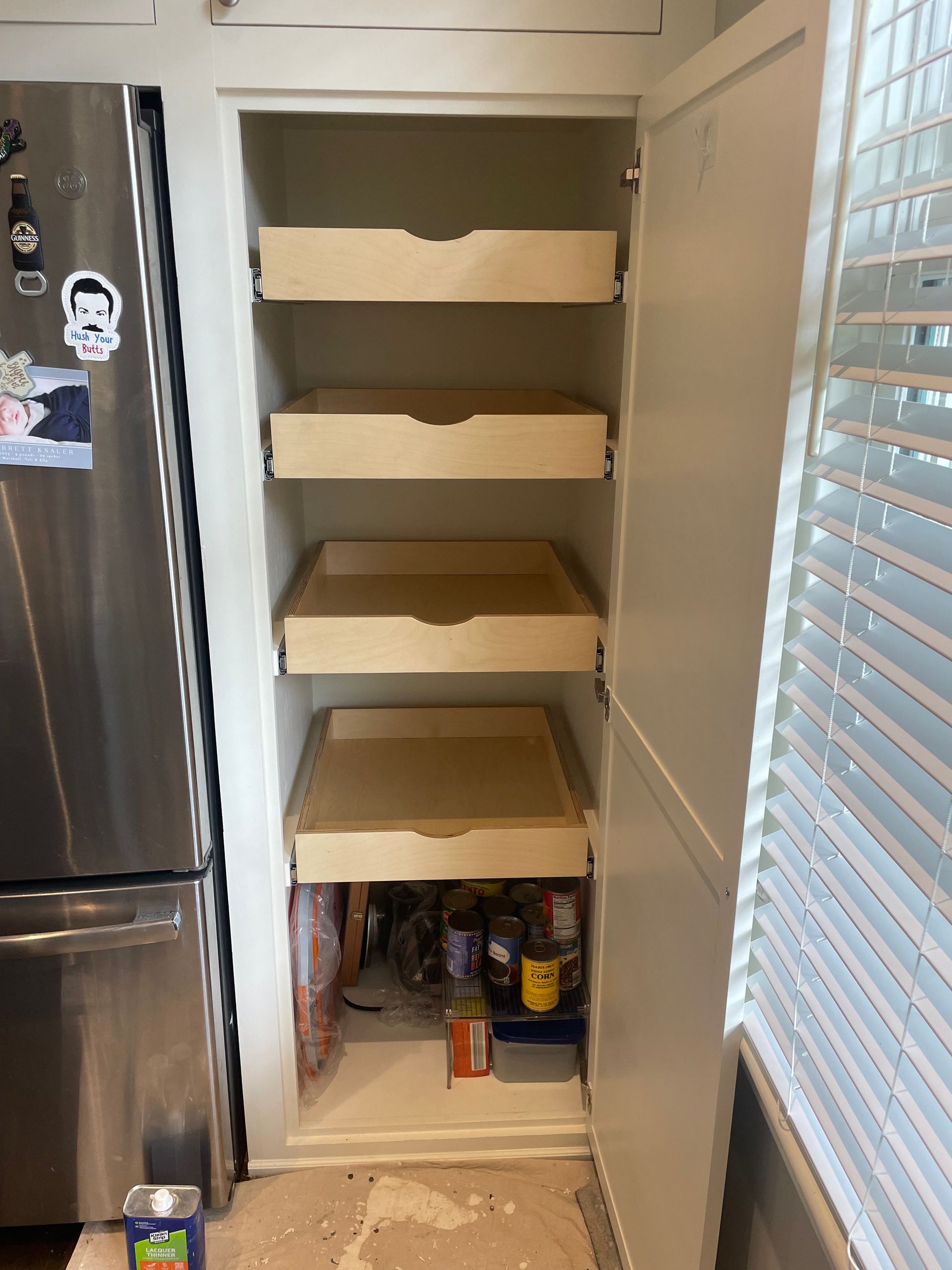 Pantry cabinet with pull-out drawers. Drawers are mostly empty. Lower shelf with food items. Stainless steel refrigerator visible.