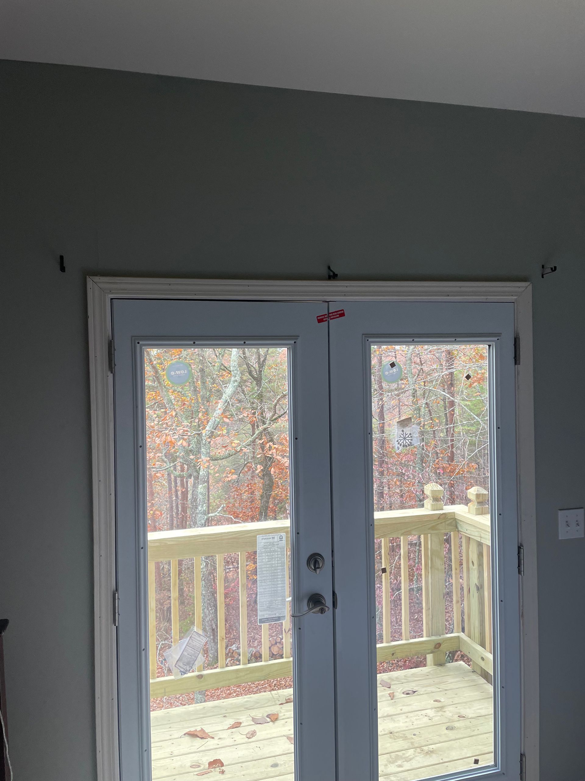 Exterior double doors with white trim and view of a wooden deck and trees.