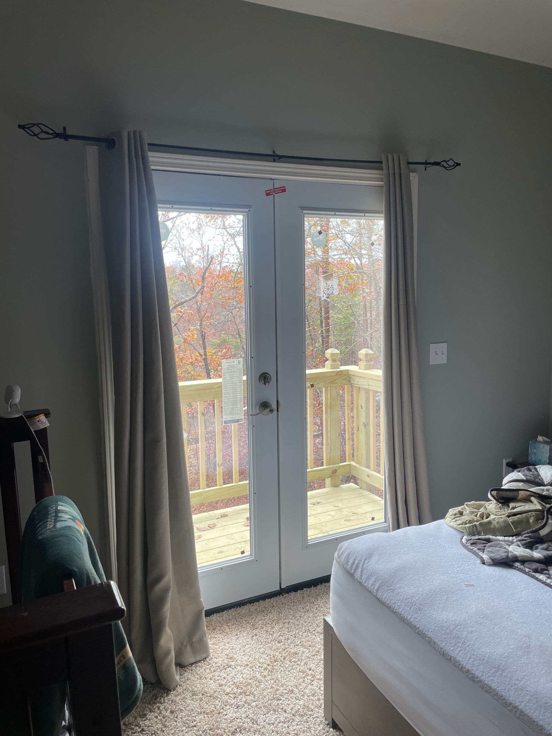 Bedroom with French doors leading to a wooden deck, light curtains, and a bed.