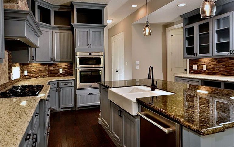 A kitchen with gray cabinets , granite counter tops , a sink , and a stove.