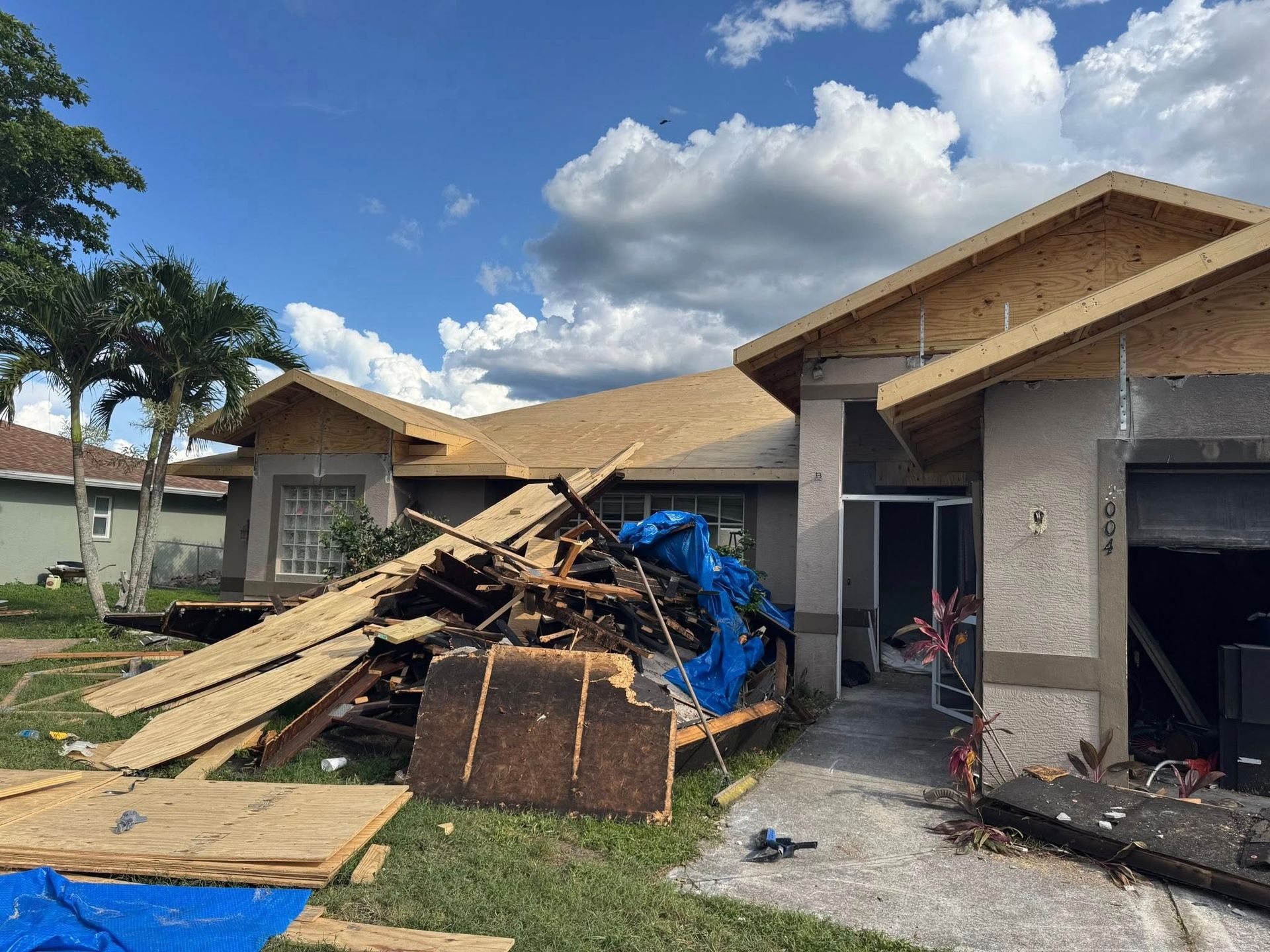 House under construction with exposed roof and pile of wood debris in front.