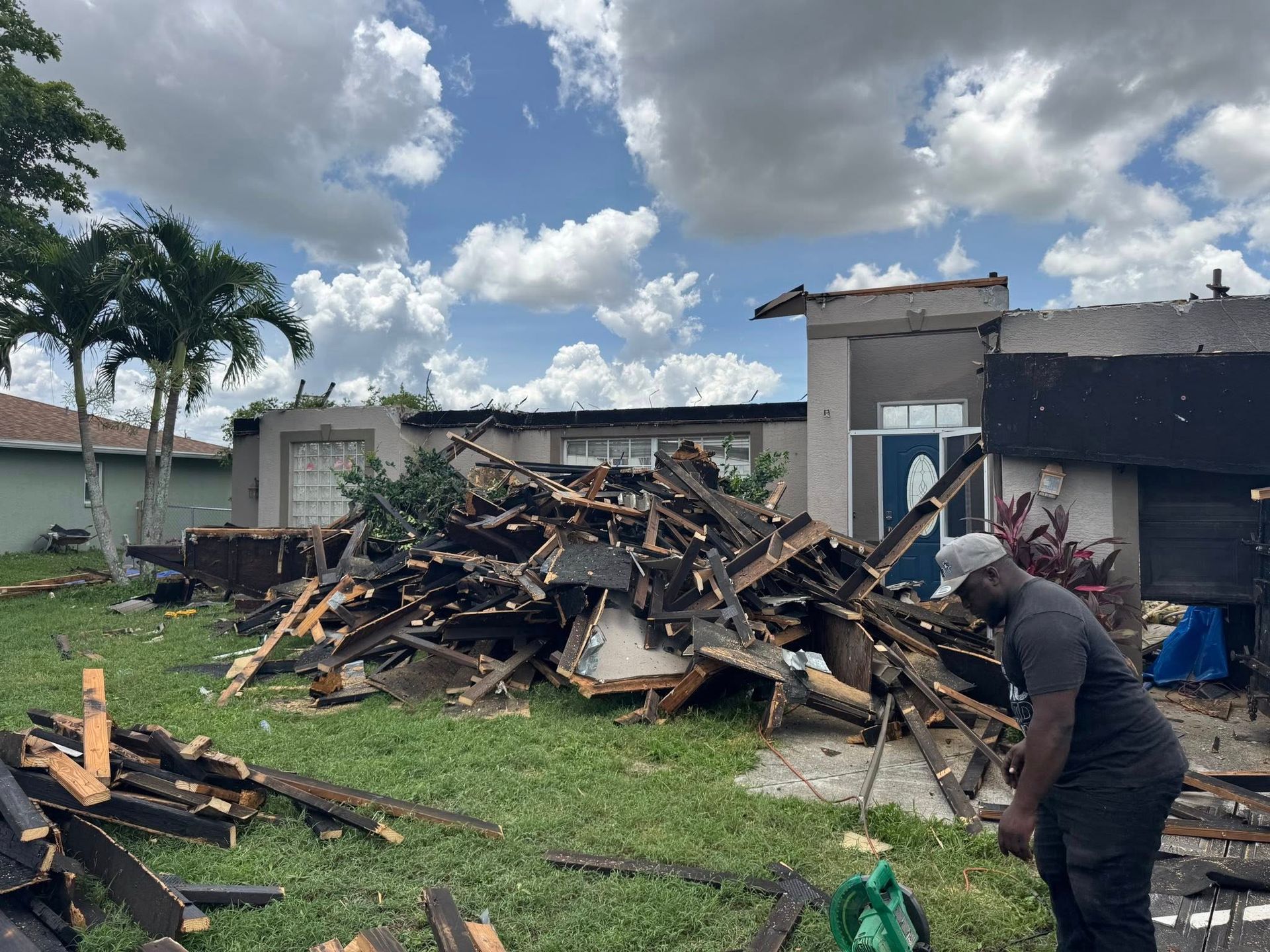 Debris from a damaged home on a lawn, with a person inspecting the wreckage under a cloudy sky.