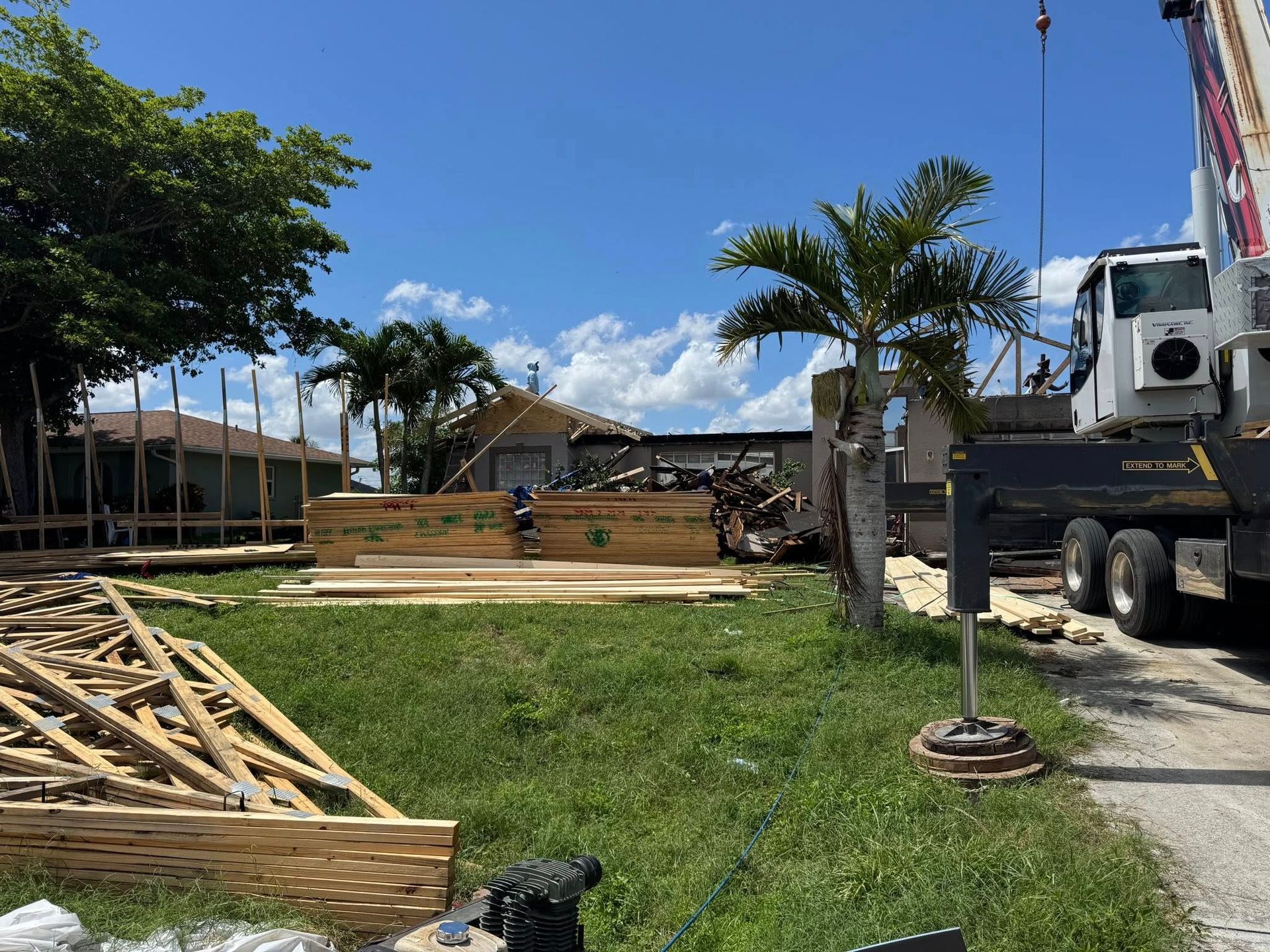 Construction site: lumber, crane, partial house under construction, green grass, blue sky.