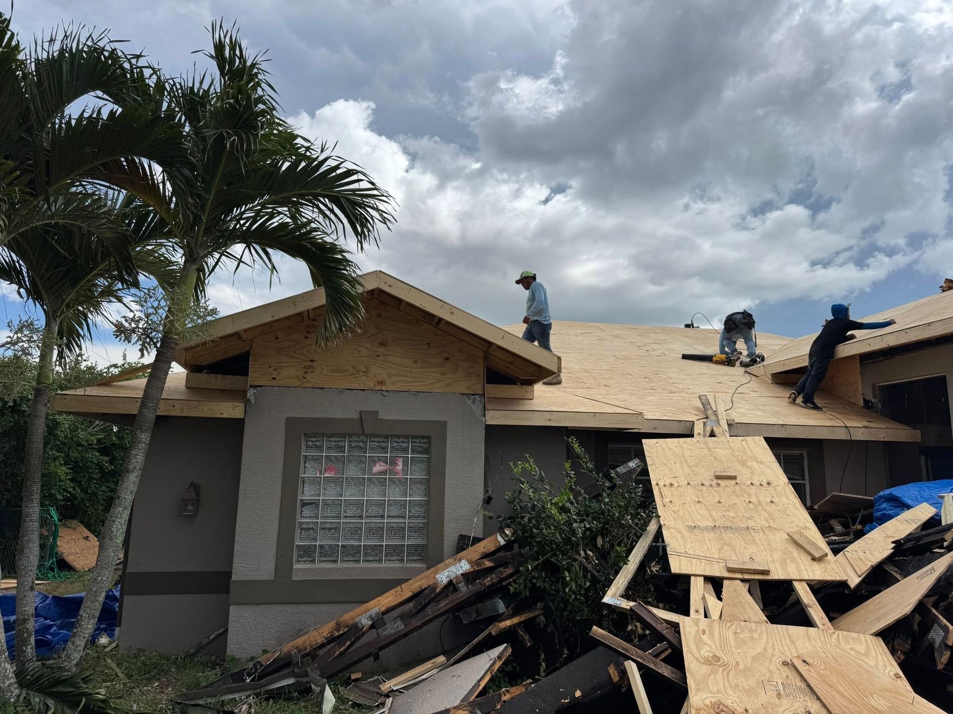 Roofers working on a house with plywood and debris.