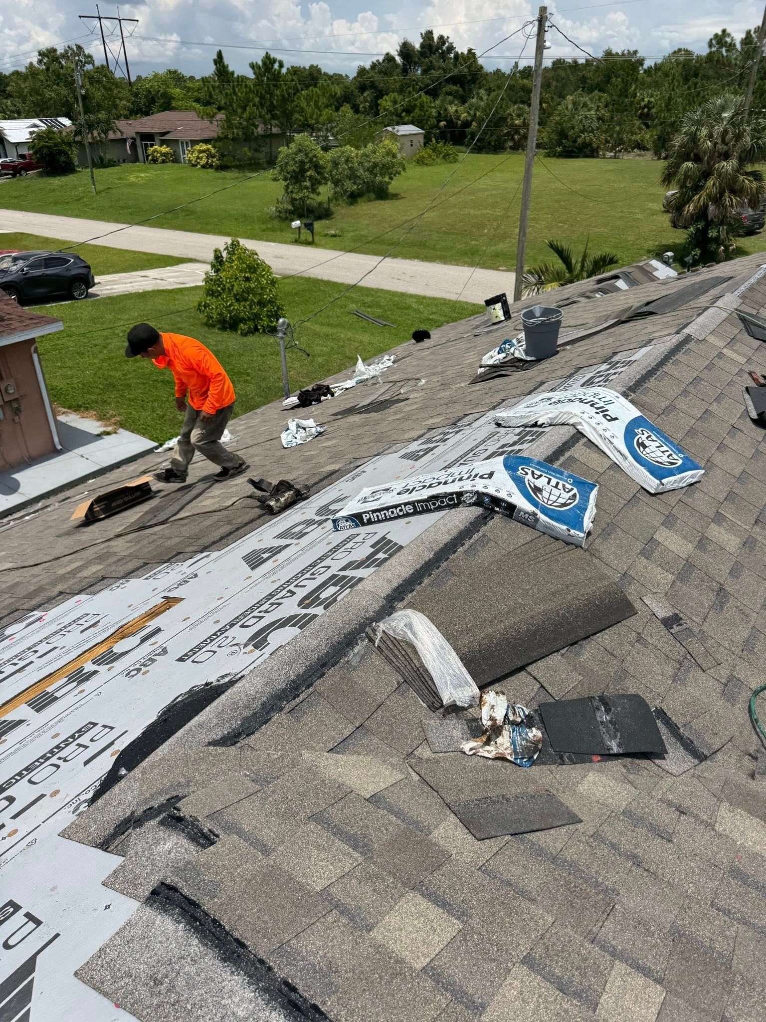 Roofer in orange shirt repairs a damaged roof, tearing off material.