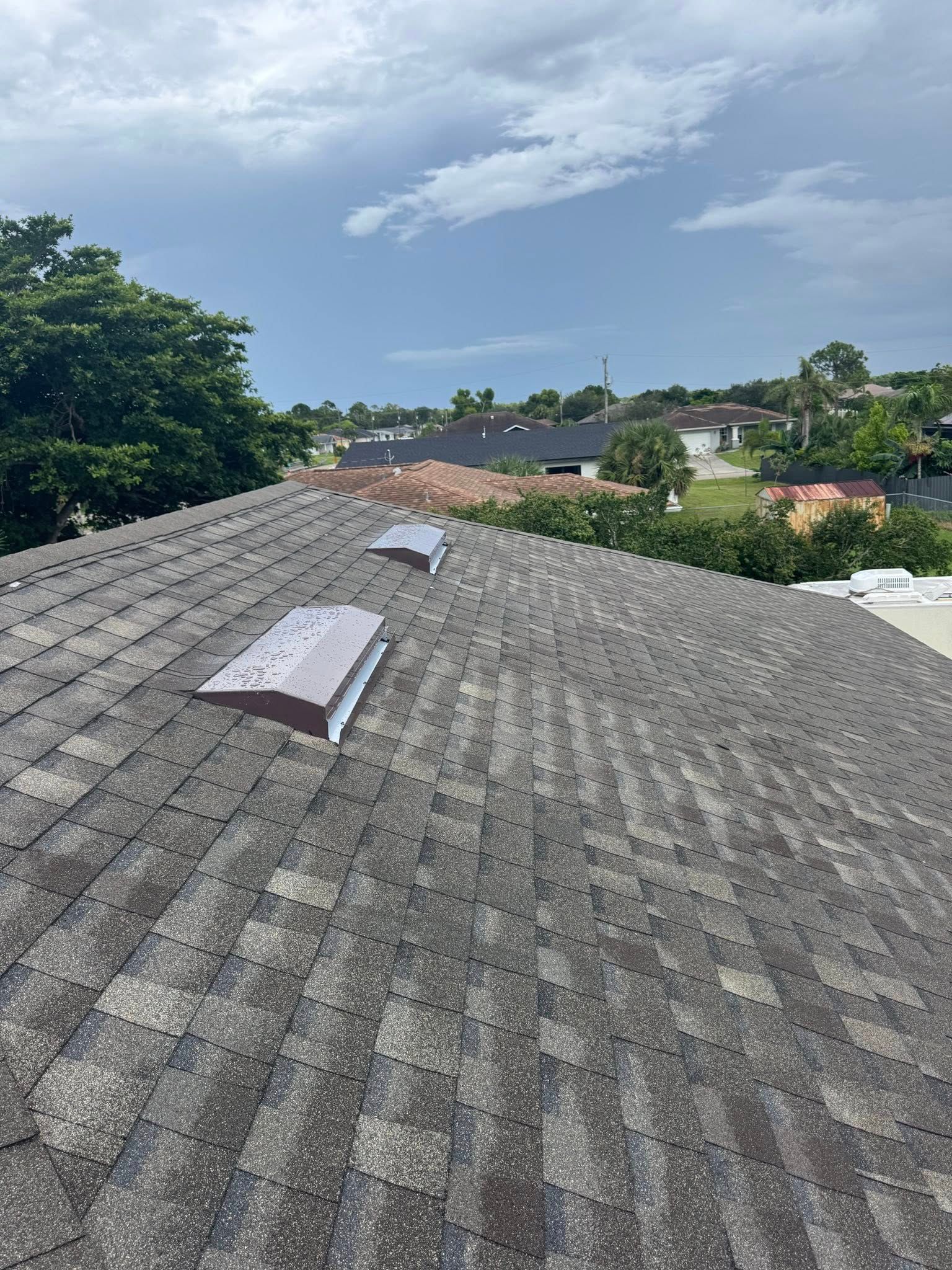 View of an asphalt shingle roof with two skylights; cloudy sky in the background.