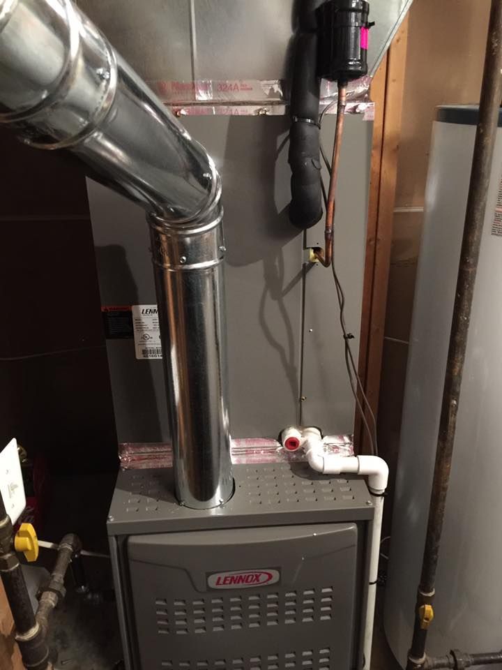 A lennox air conditioner is sitting in a basement next to a water heater.