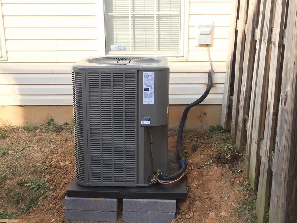 An air conditioner is sitting on top of a concrete block in the backyard of a house.