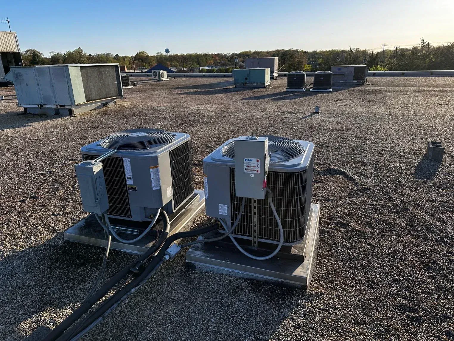 Two air conditioners are sitting on top of a gravel roof.