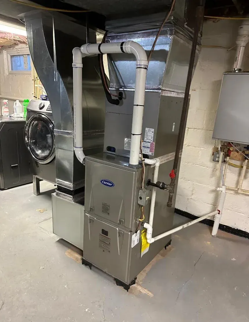 A stainless steel furnace is sitting in a basement next to a washer and dryer.
