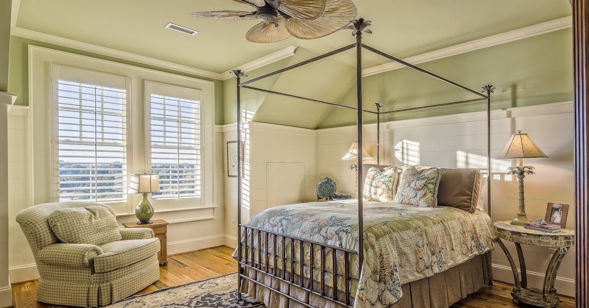 A bedroom with a canopy bed , chair , lamps and a ceiling fan.