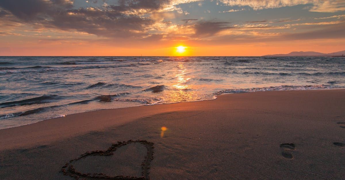 A heart is drawn in the sand on the beach at sunset.