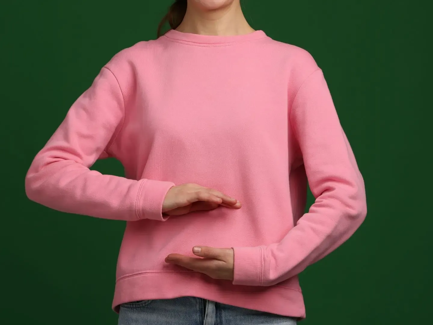 Person in pink sweatshirt, hands framing midsection. Green background.