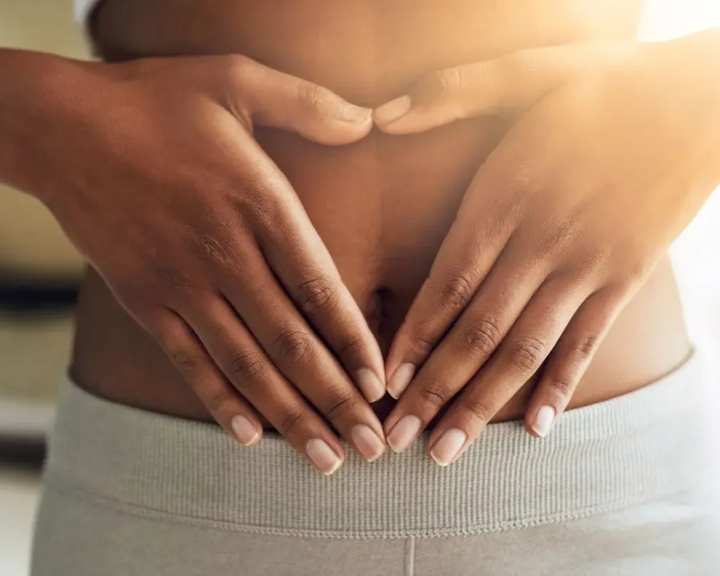 Hands forming a heart over a person's abdomen, wearing light-colored athletic attire.
