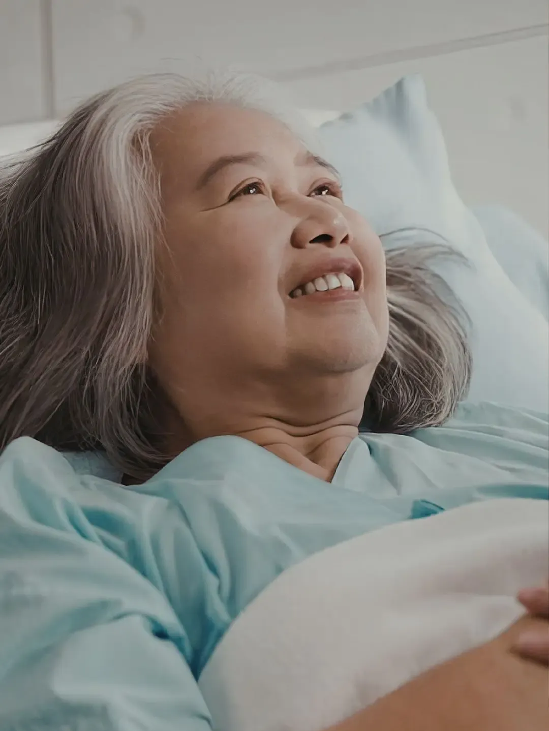 Smiling person in a hospital bed, wearing a hospital gown and looking up.