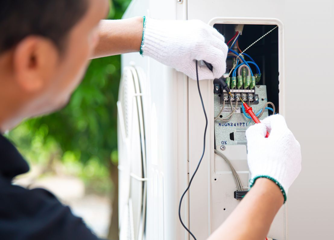 A Man Is Working On An Air Conditioner — Chris North Electrical In Jones Hill, QLD