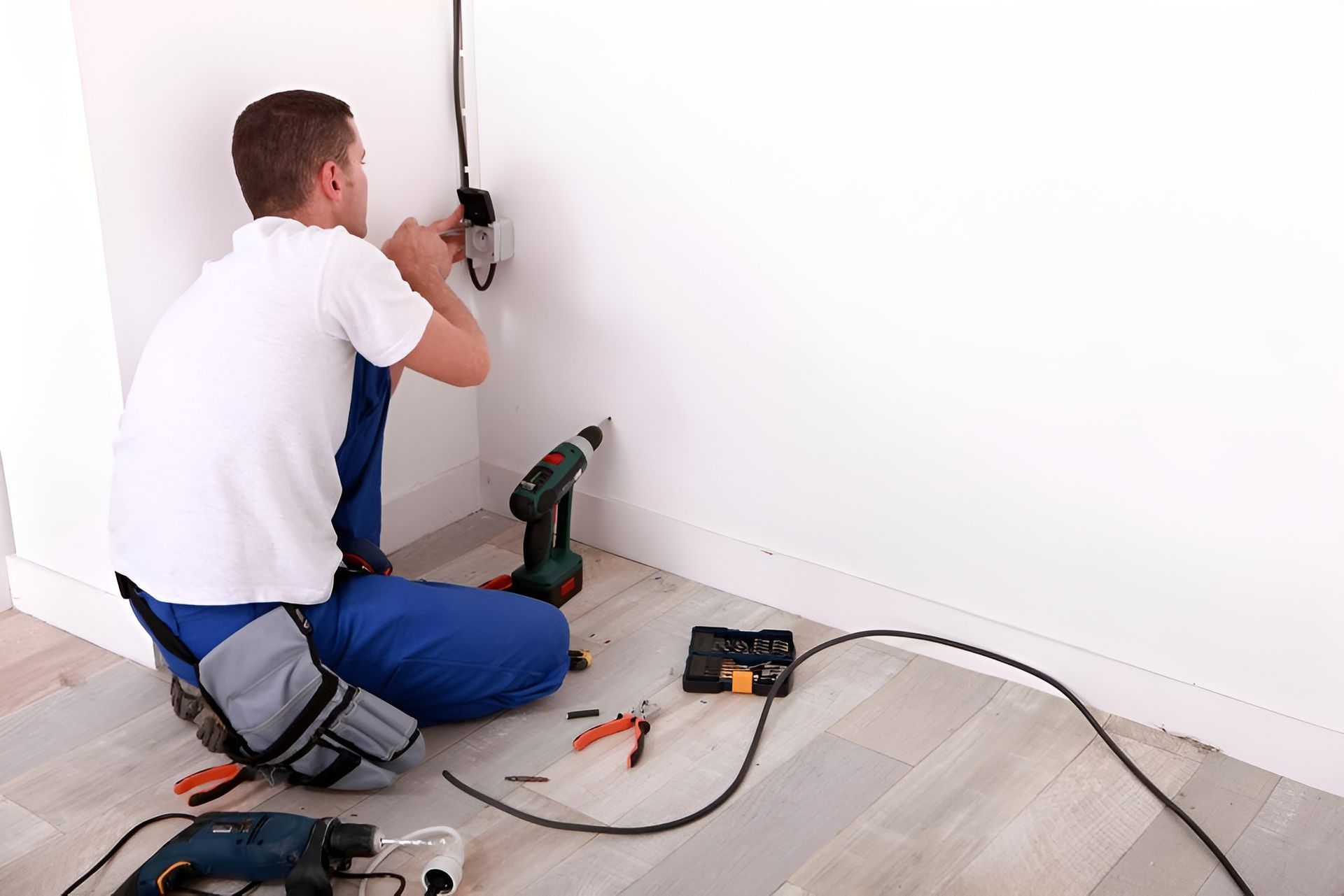 A Man Is Sitting On The Floor Working On A Wall — Chris North Electrical In Jones Hill, QLD