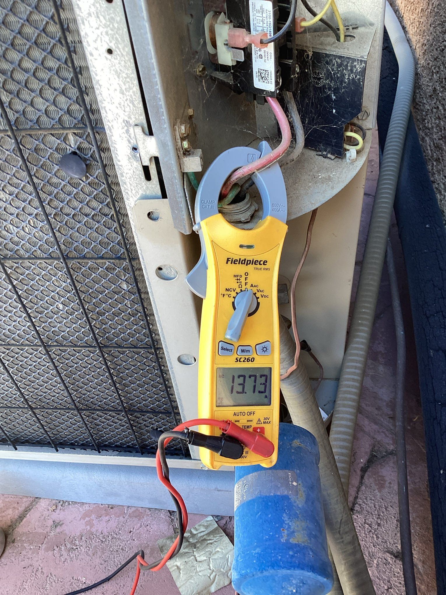 A clamp meter measures amperage on an AC unit. The display reads 137.3. Wires and electrical components are visible.