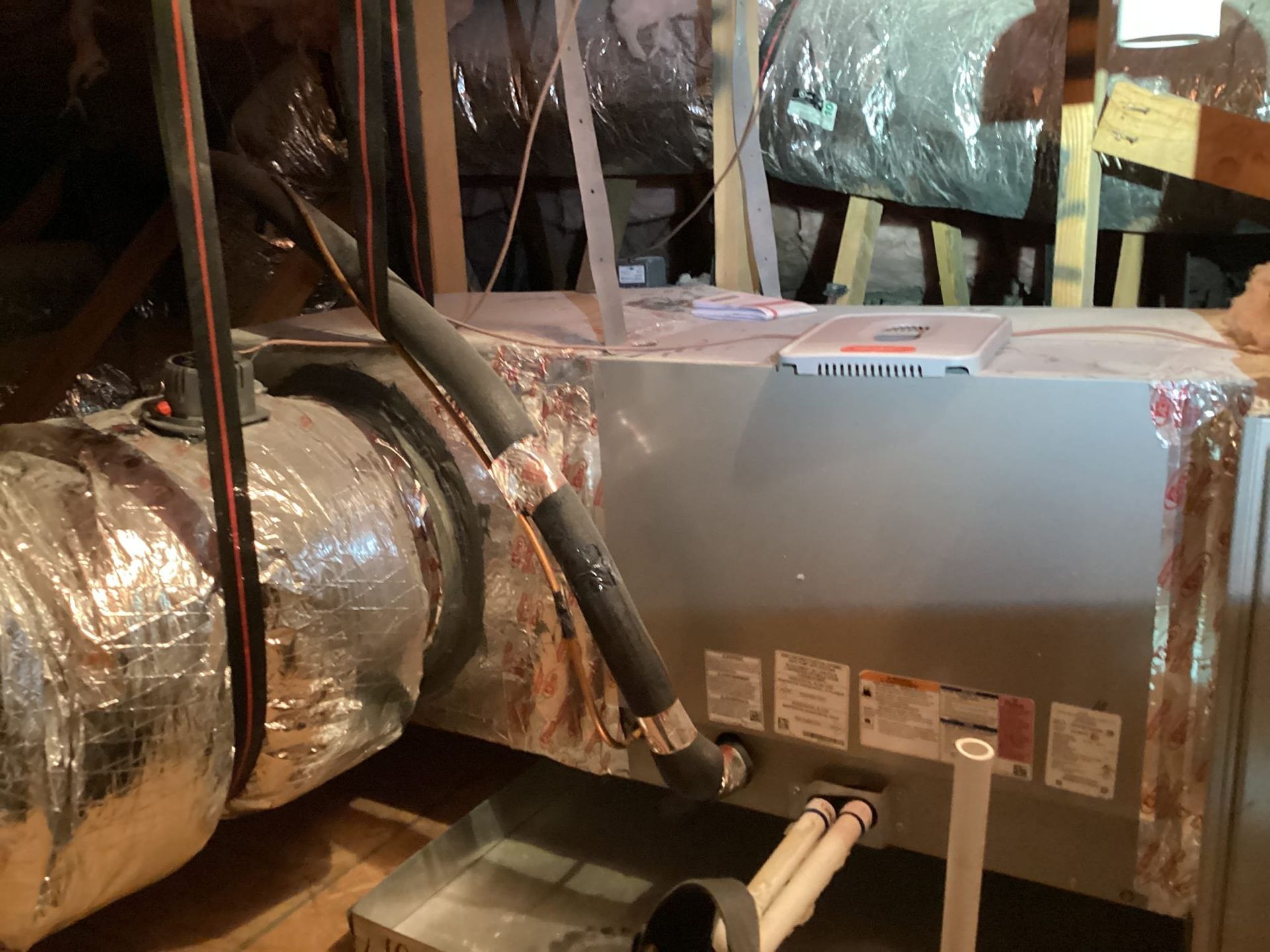 HVAC unit in an attic with insulated ductwork and a condensation drain pan.