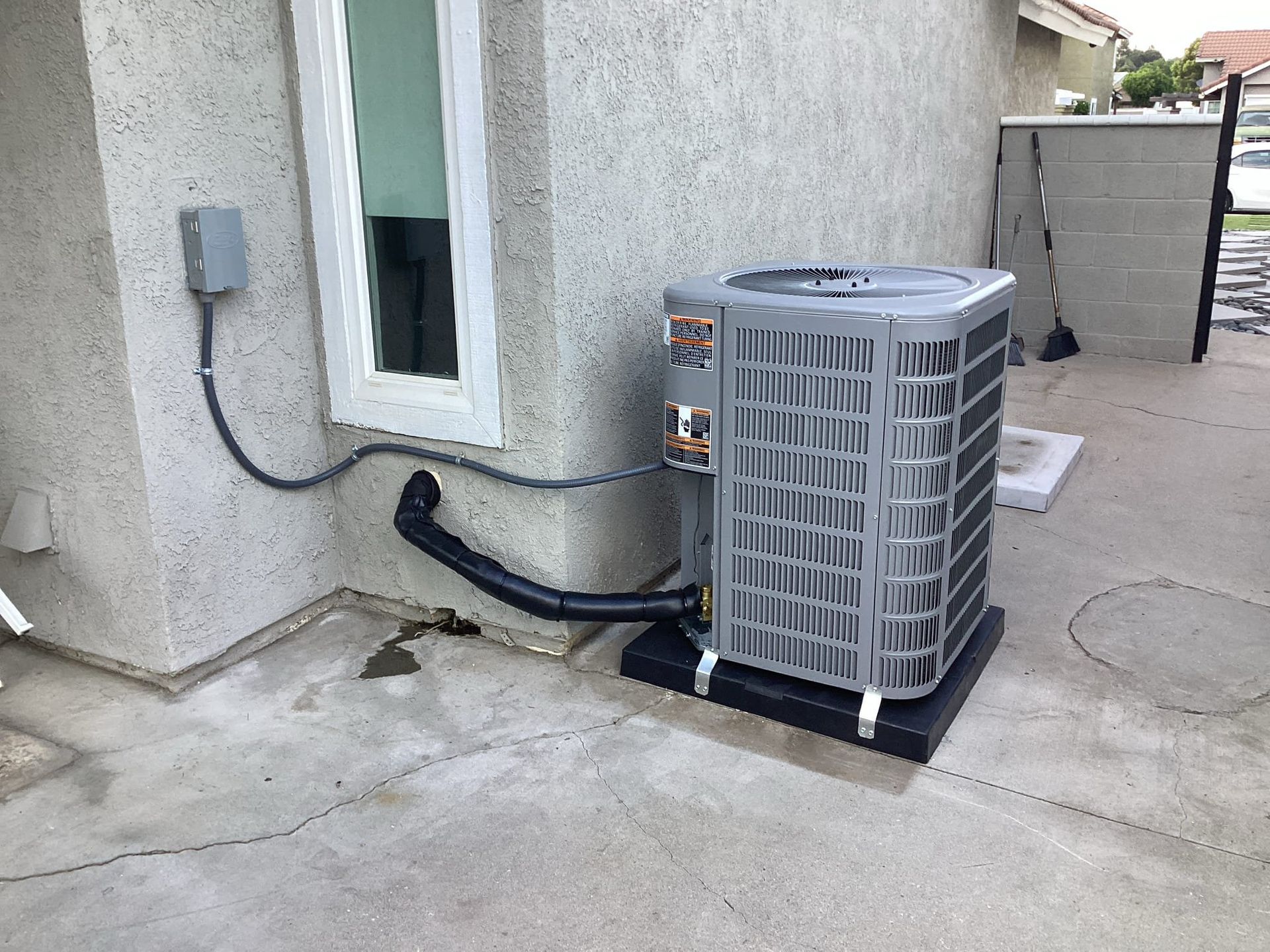 Air conditioning unit outside a stucco building near a window and electrical box.