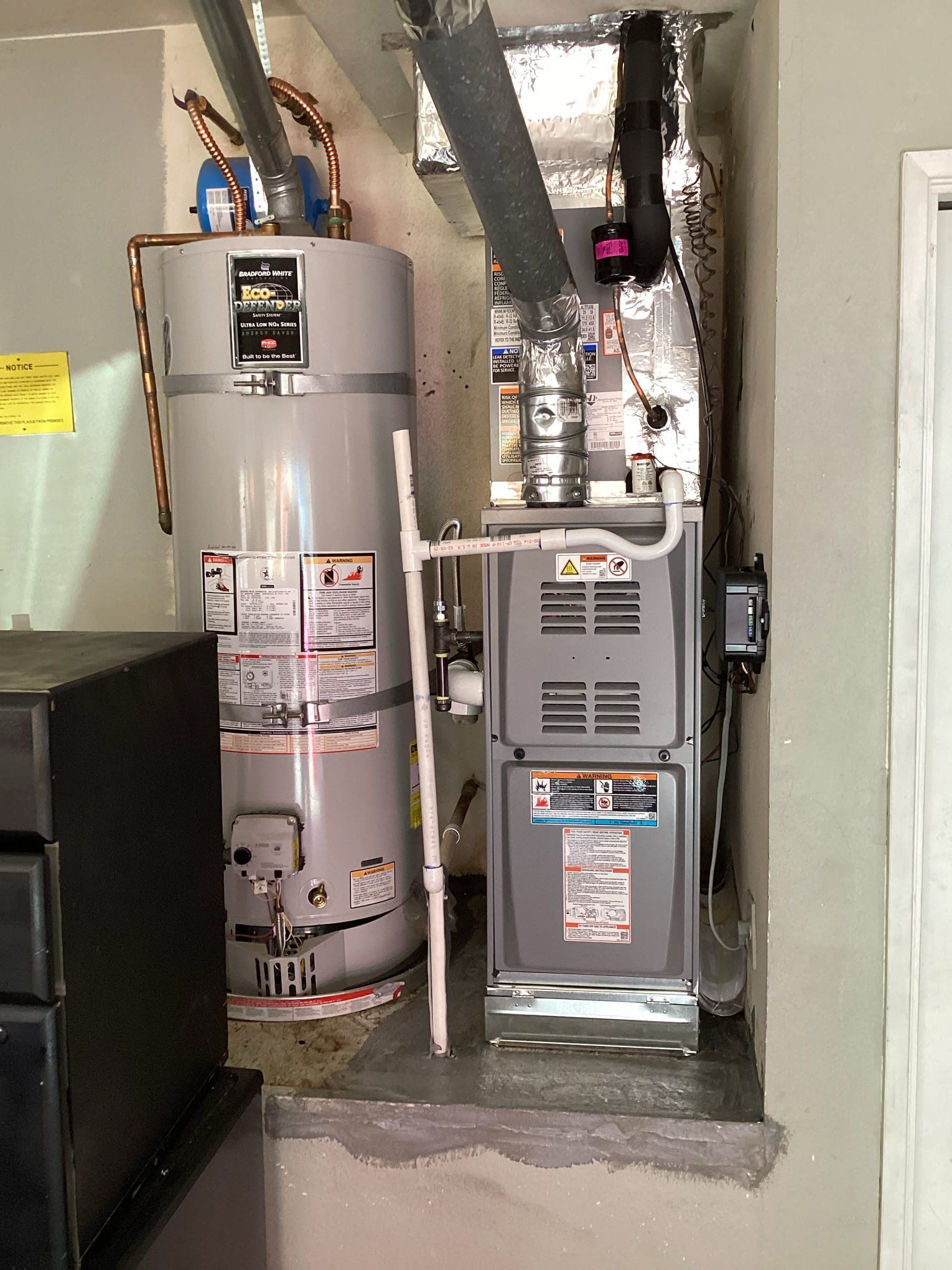 Water heater and HVAC unit in a utility room. Gray metal appliances against a neutral wall.