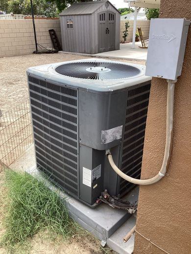 Air conditioning unit outdoors next to a building; a gray shed is in the background.