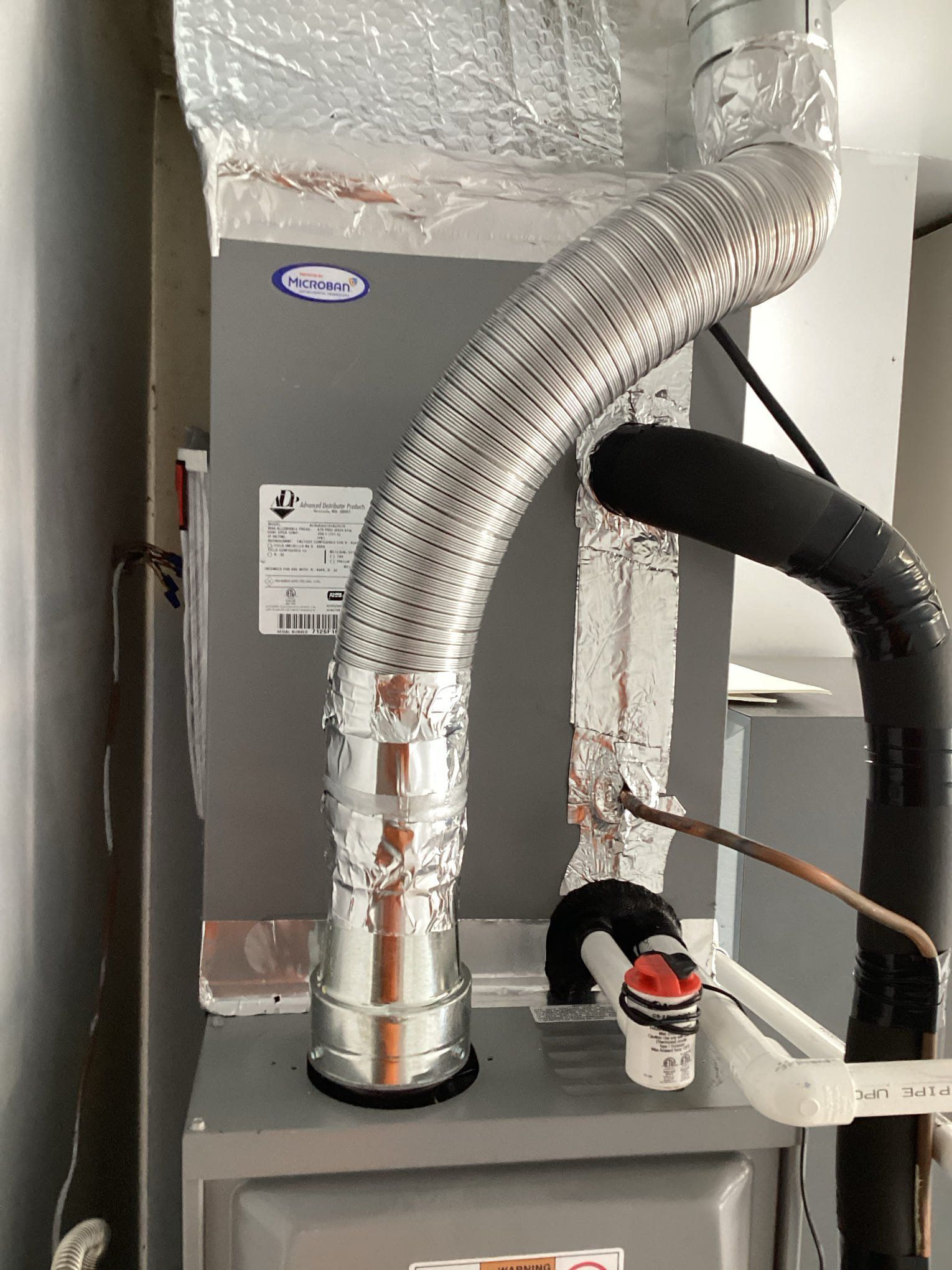HVAC unit with silver flexible ductwork and black pipe, set against a wall.