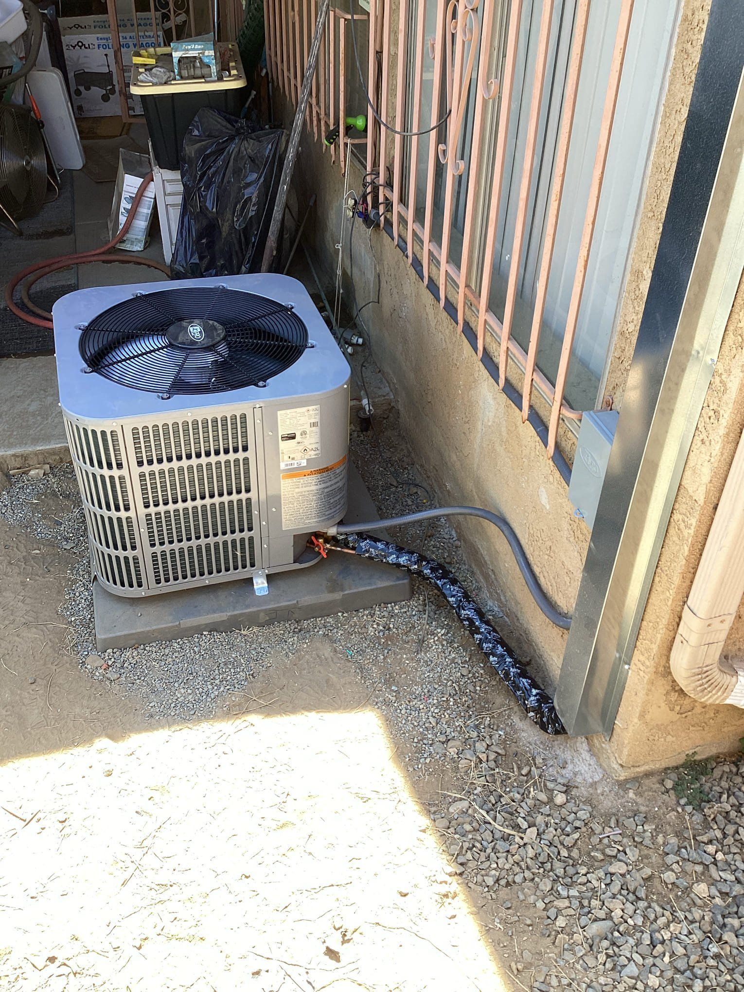 Air conditioning unit next to a building, with insulated pipes running toward a wall.