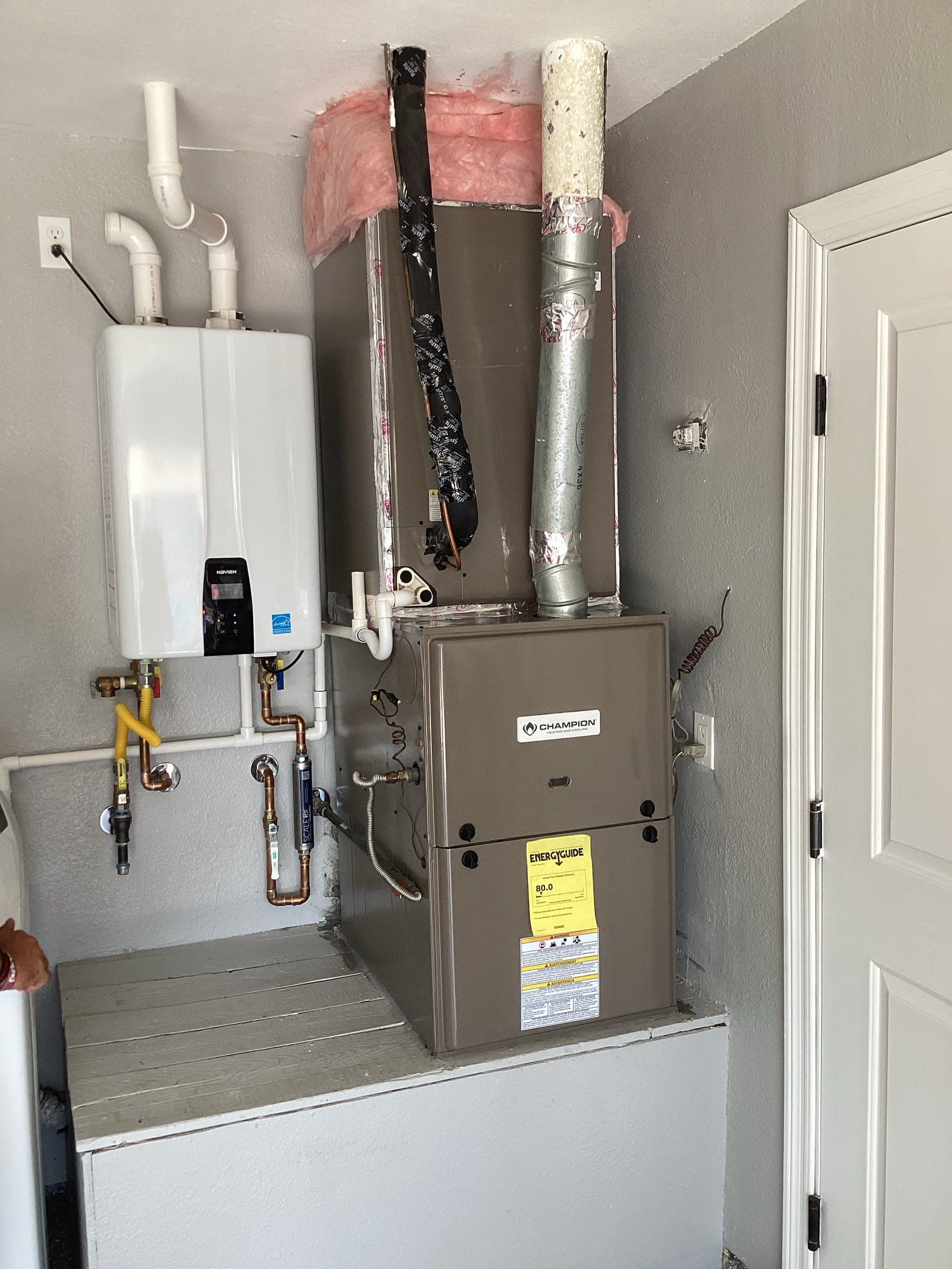 Furnace, water heater, and ductwork installed in a utility closet with white door and gray walls.