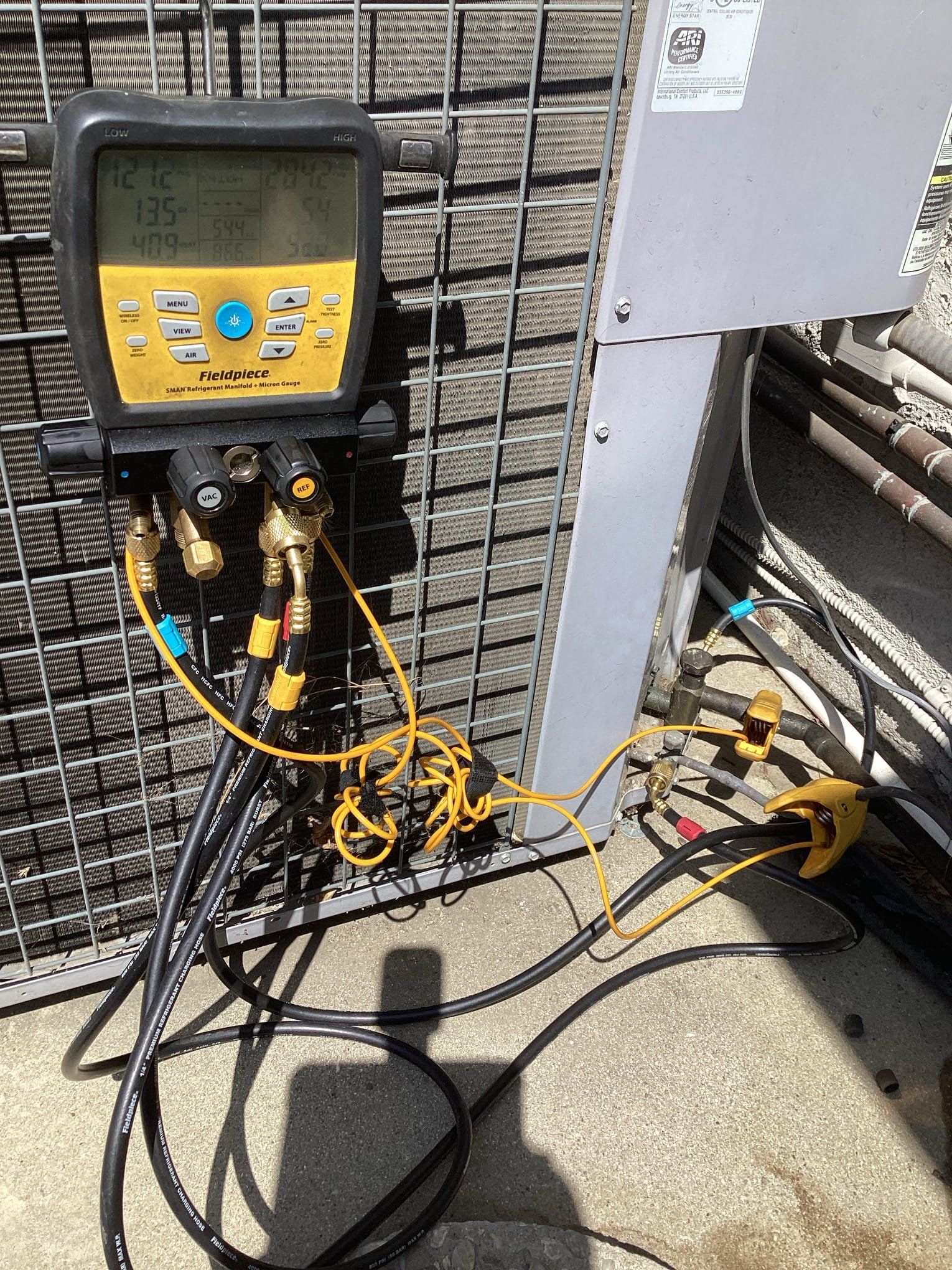 HVAC technician using yellow and black digital manifold on an outdoor air conditioning unit.