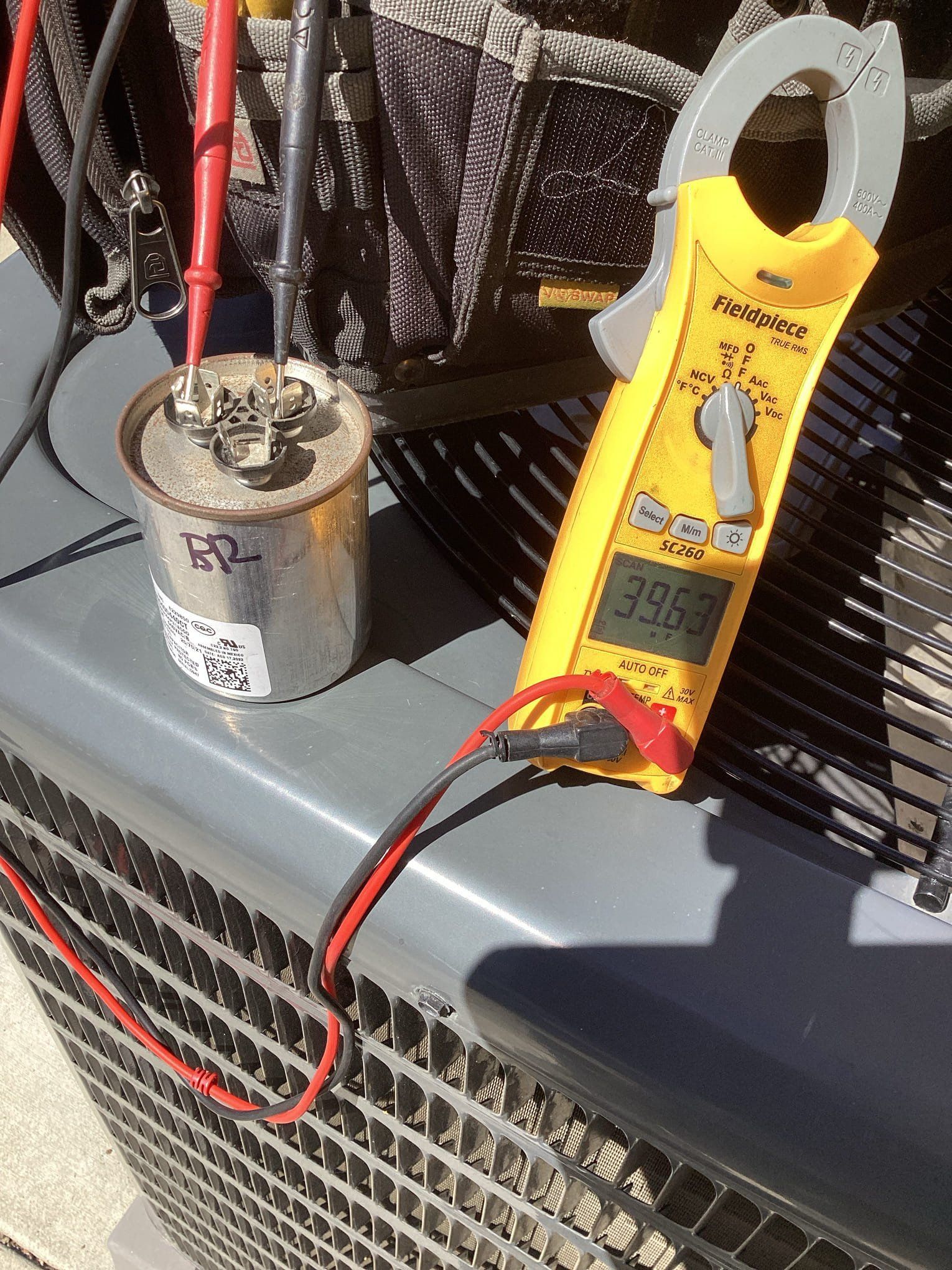 A technician tests a capacitor with a multimeter on an air conditioning unit.