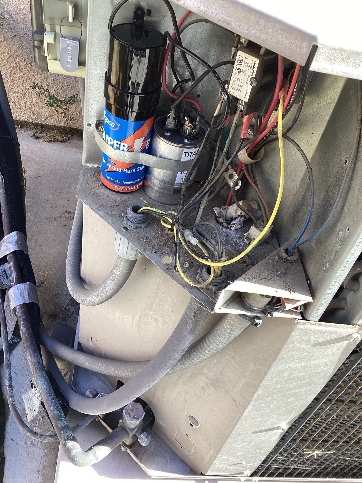 Open electrical components of an air conditioning unit. Wiring, capacitors, and contactors are visible.